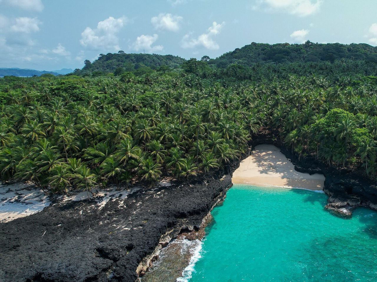 Playa desierta con rocas volcánicas alrededor, agua cristalina y palmeras rodeando la playa