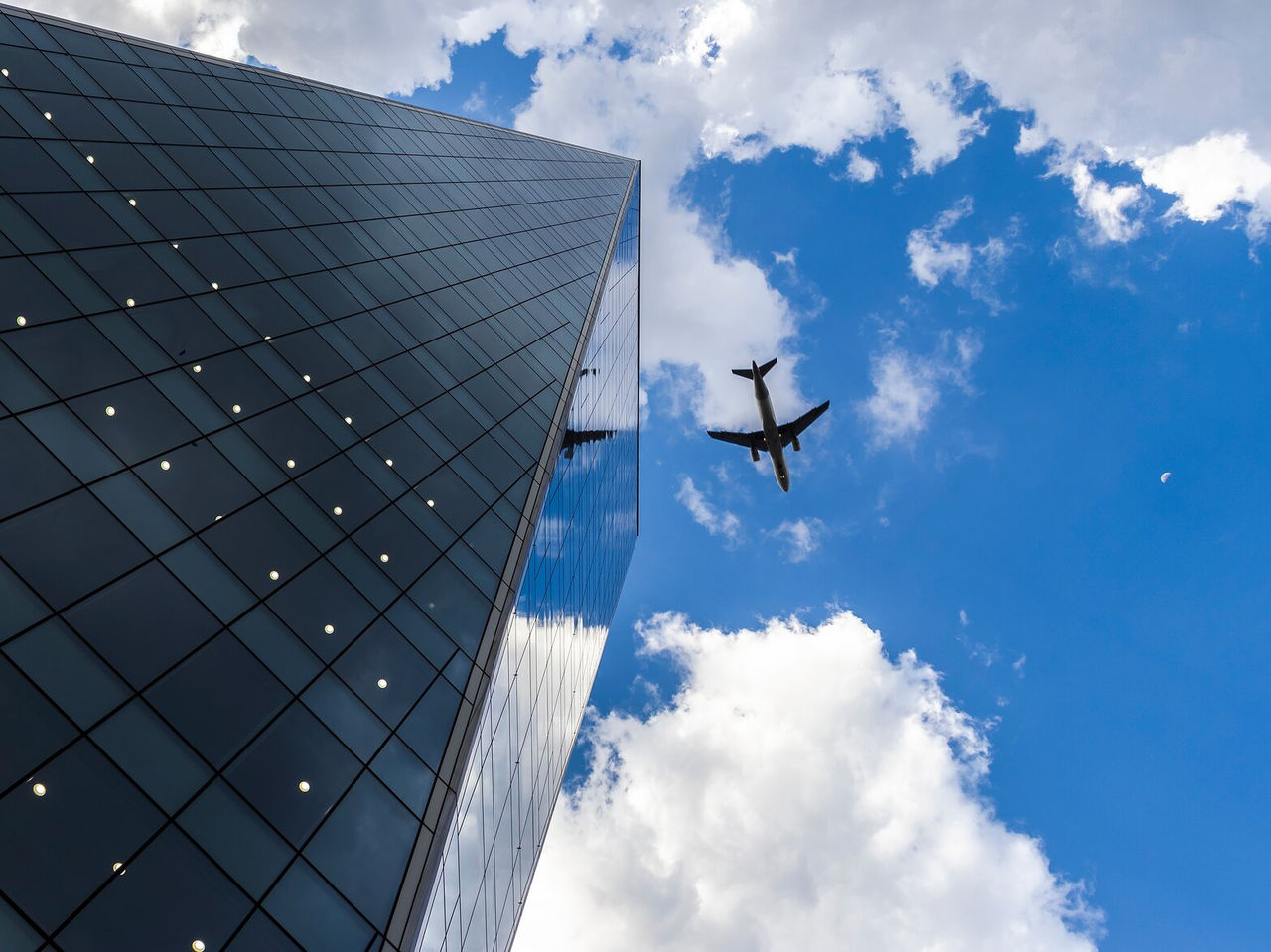 Fachada de vidrio de un edificio en São Paulo con reflejos de nubes y un avión en vuelo