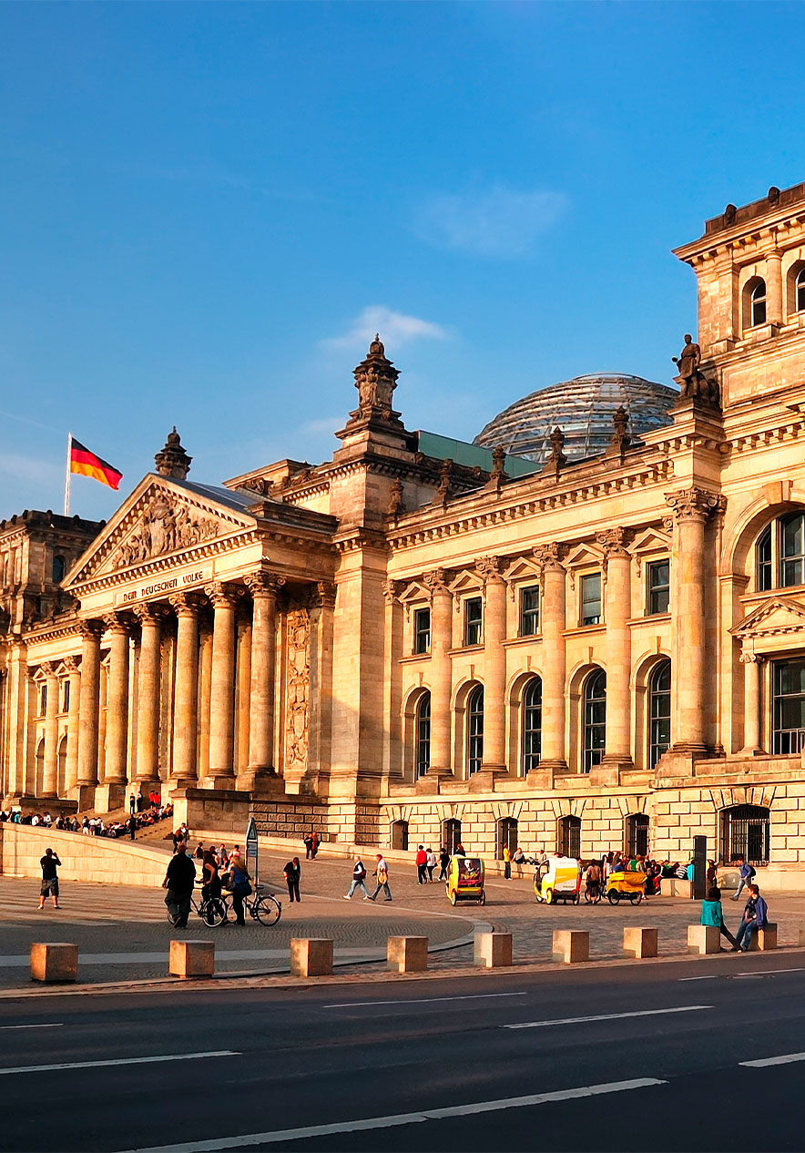 Edificio del Reichstag en Berlín al atardecer, con banderas alemanas y gente caminando