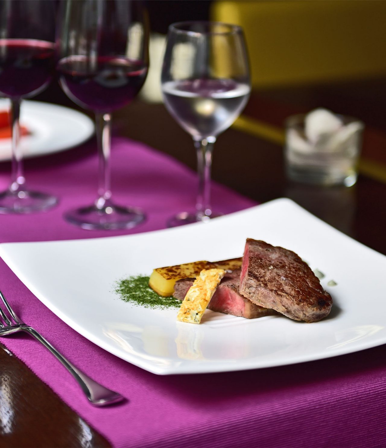 El bar Lobby, del Hotel en Barcelona, presenta un plato elegante con carne y fruta, y una copa de vino y agua