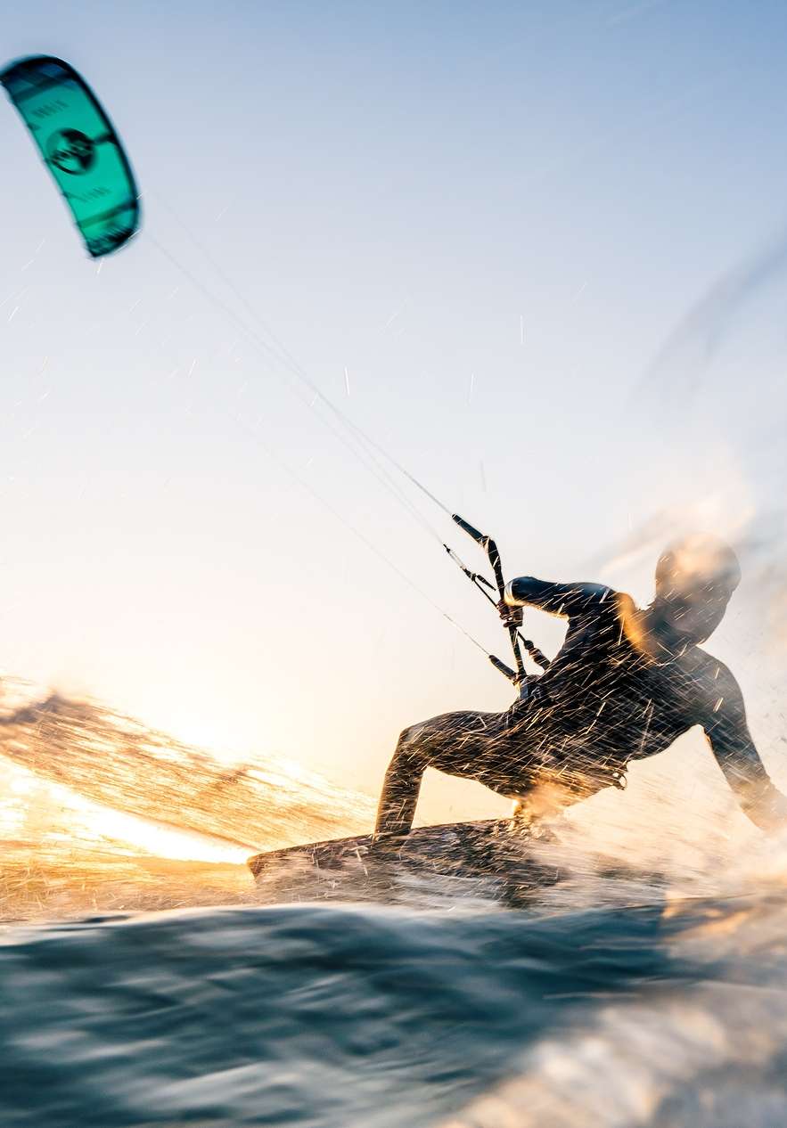 Persona haciendo kitesurf en una playa en un día soleado, con cielo azul y agua clara