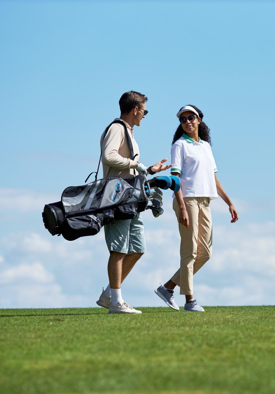 Pareja cargando tacos de golf en un campo de golf en Porto Santo, con cielo azul