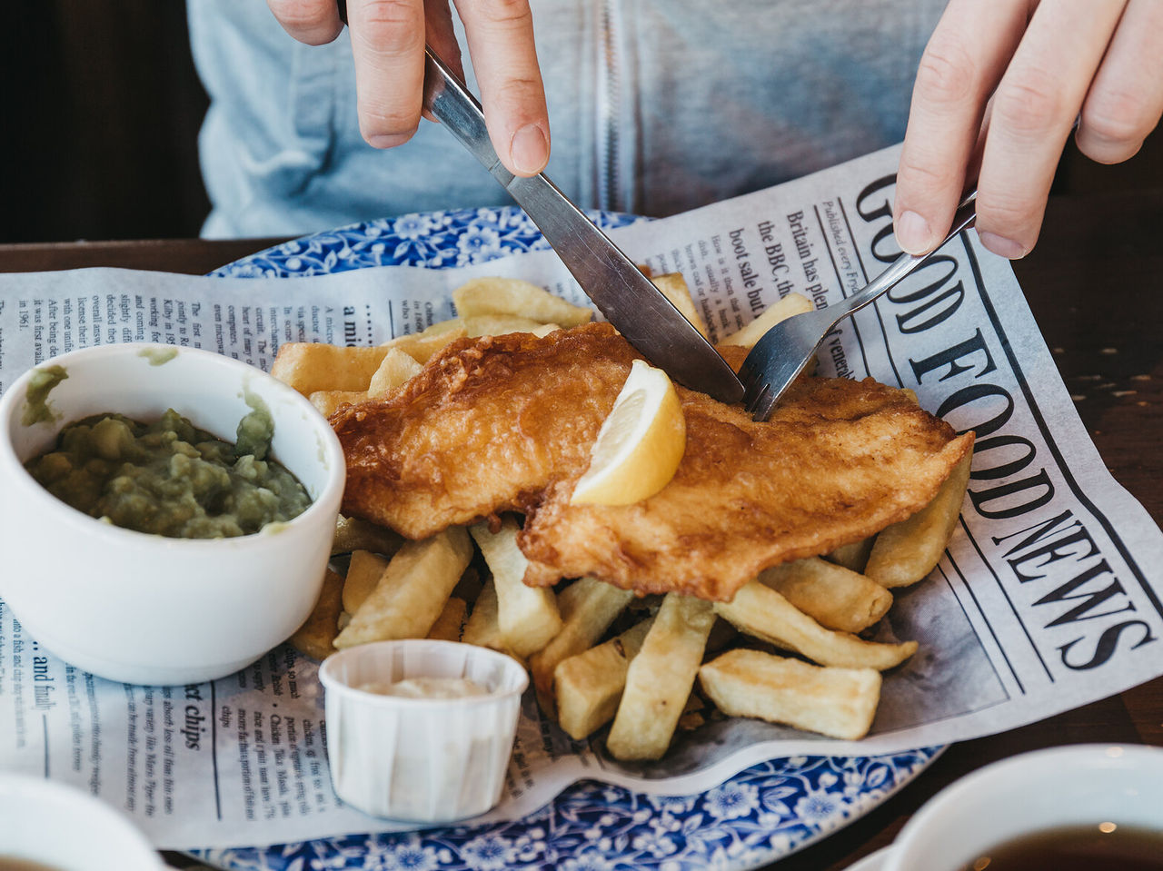 Una persona disfrutando de un plato típico inglés de fish and chips, un pescado frito acompañado de patatas fritas crujientes