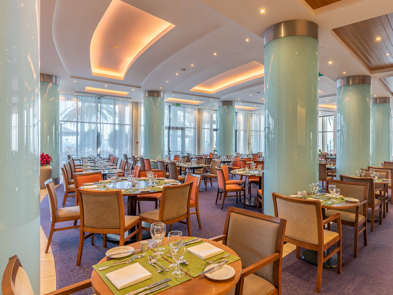O restaurante Atrium, do Hotel 5 Estrelas no Funchal, na Madeira, tem uma sala ampla, com pilares azuis, e mesas e cadeiras