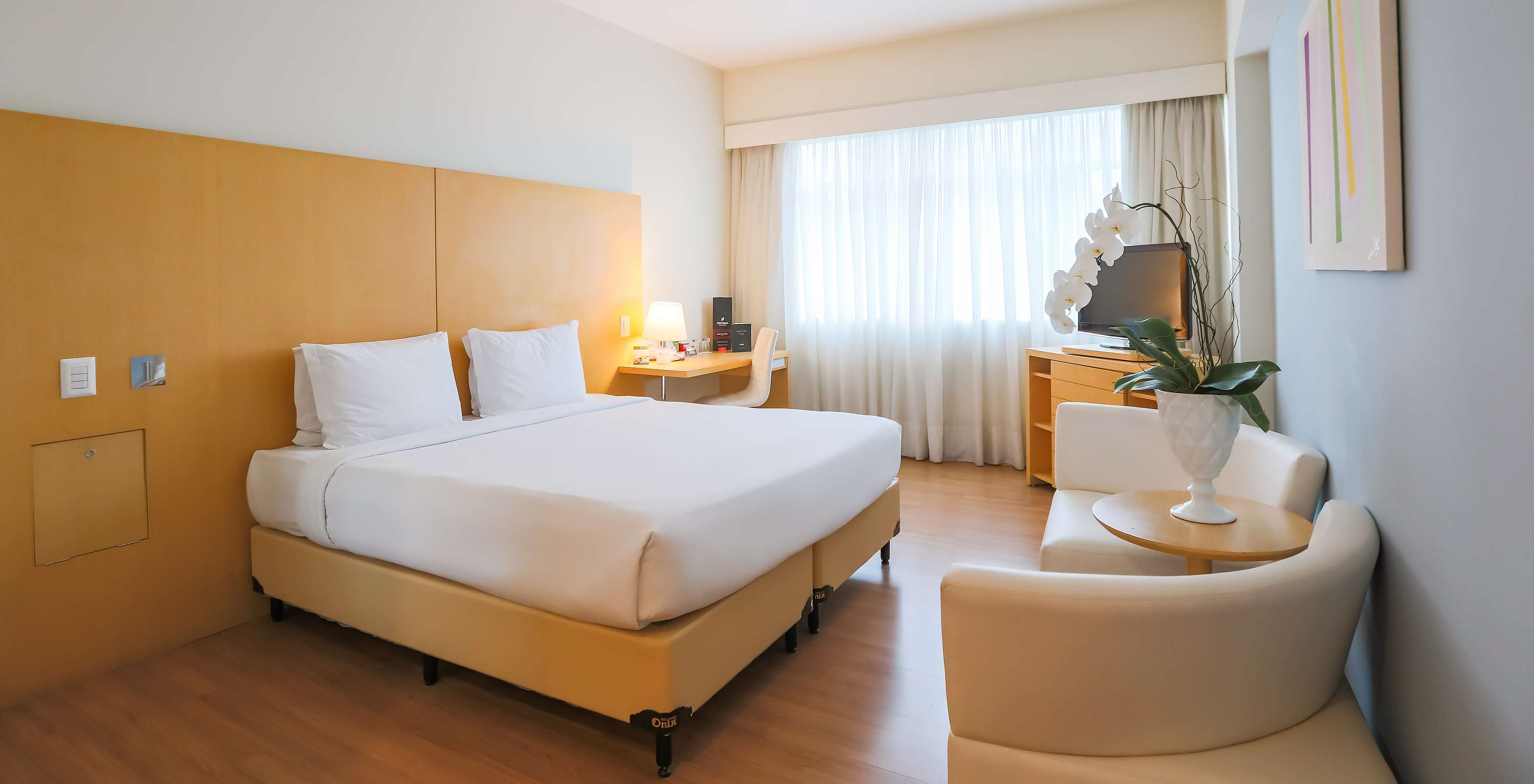 The Queen Standard at Pestana Curitiba has a room with a double bed, sofas, a desk, and a furniture unit with a TV