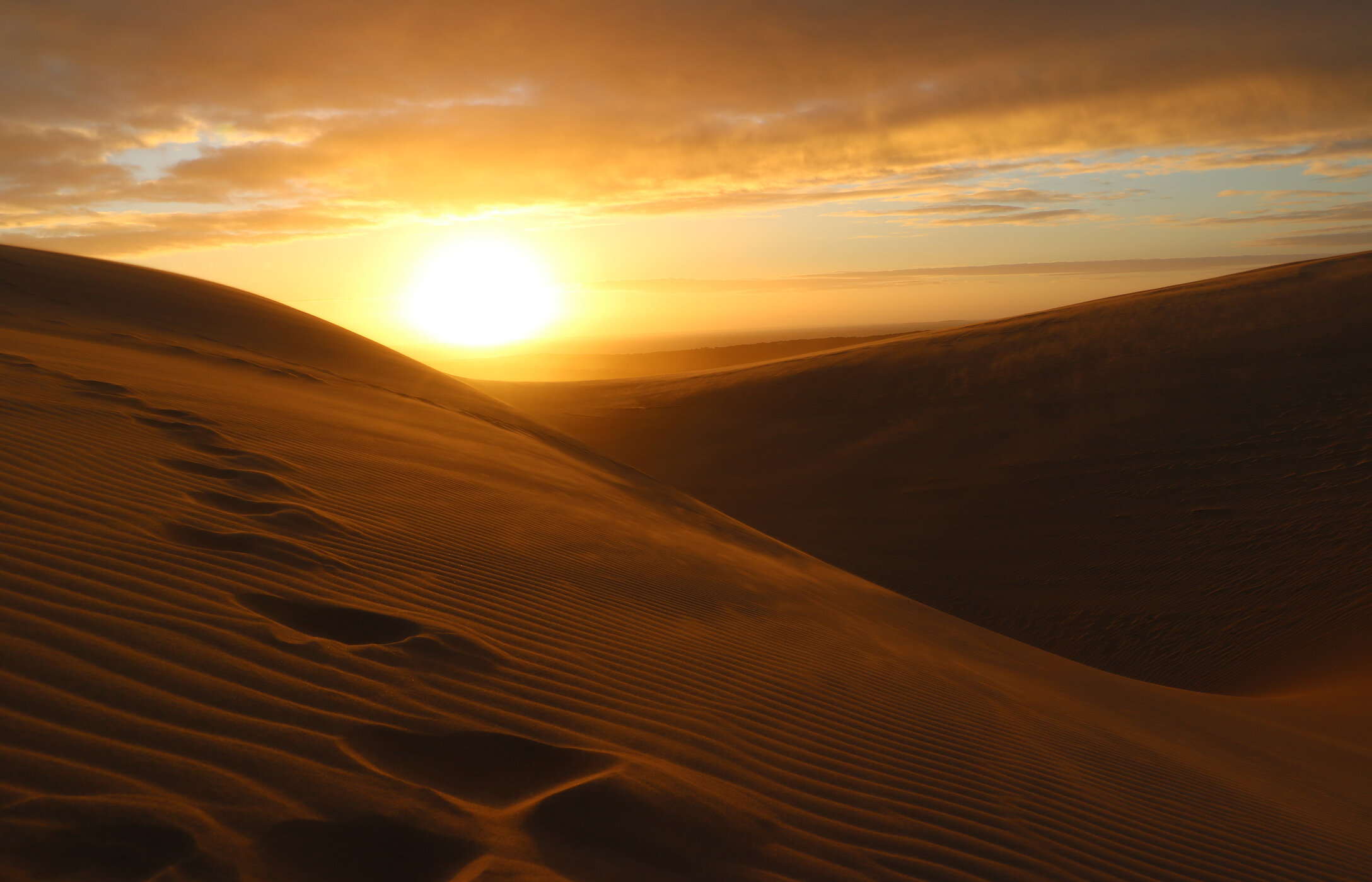 Panoramic view of the sand dunes in Bazaruto, with the sun setting on the horizon and a sky in warm tones