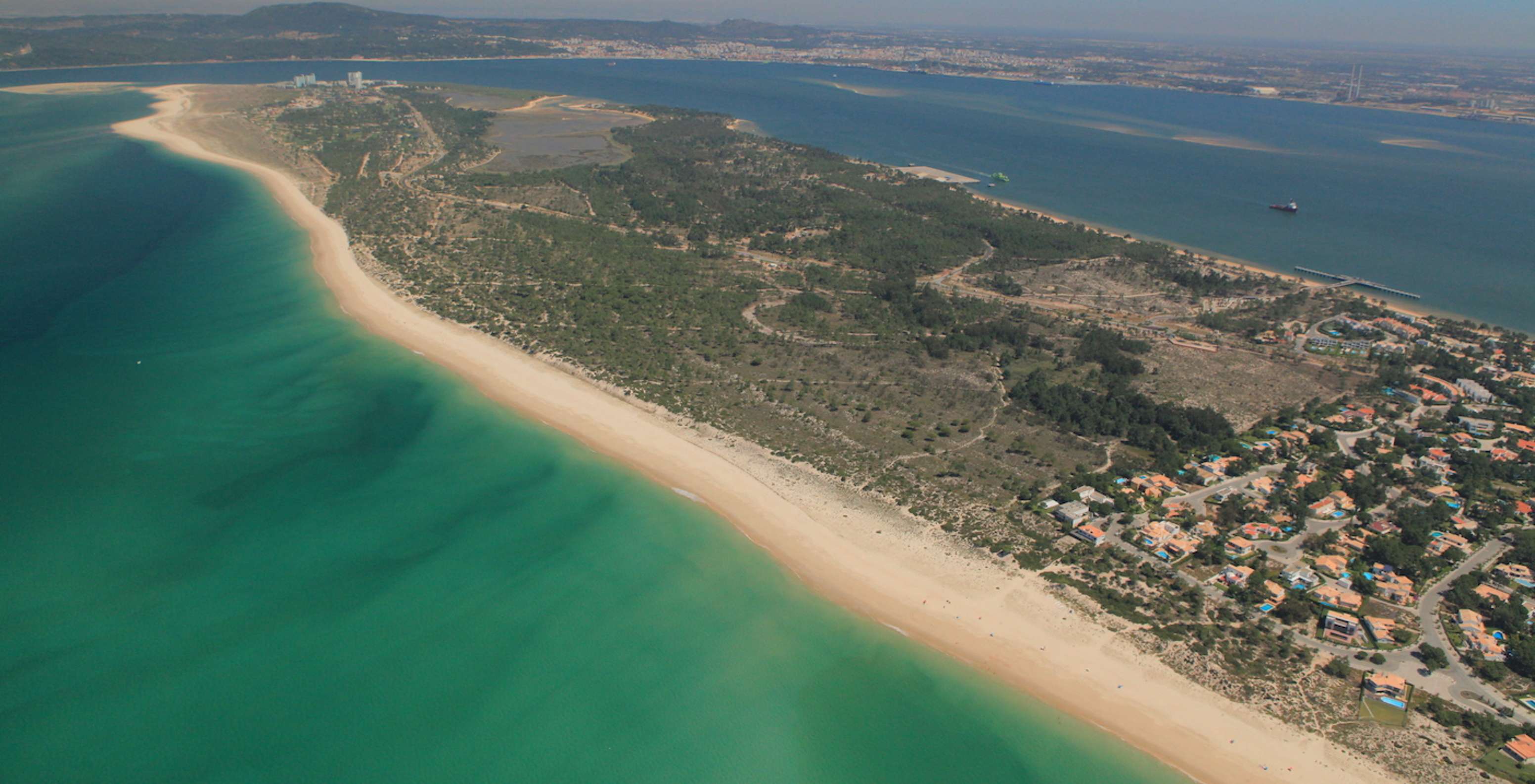 Aerial view of the Tróia Peninsula, with clear water, lush greenery, and various houses with pools