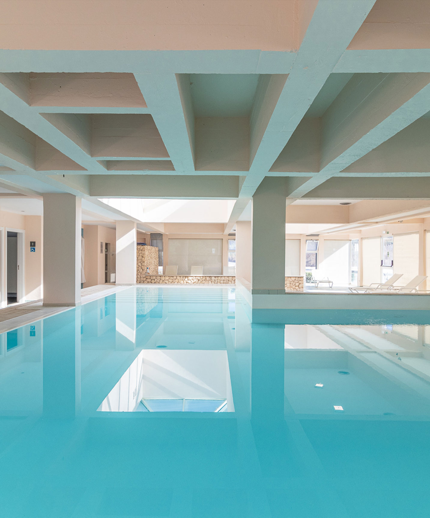 Indoor pool with natural light and loungers at aparthotel by the sea