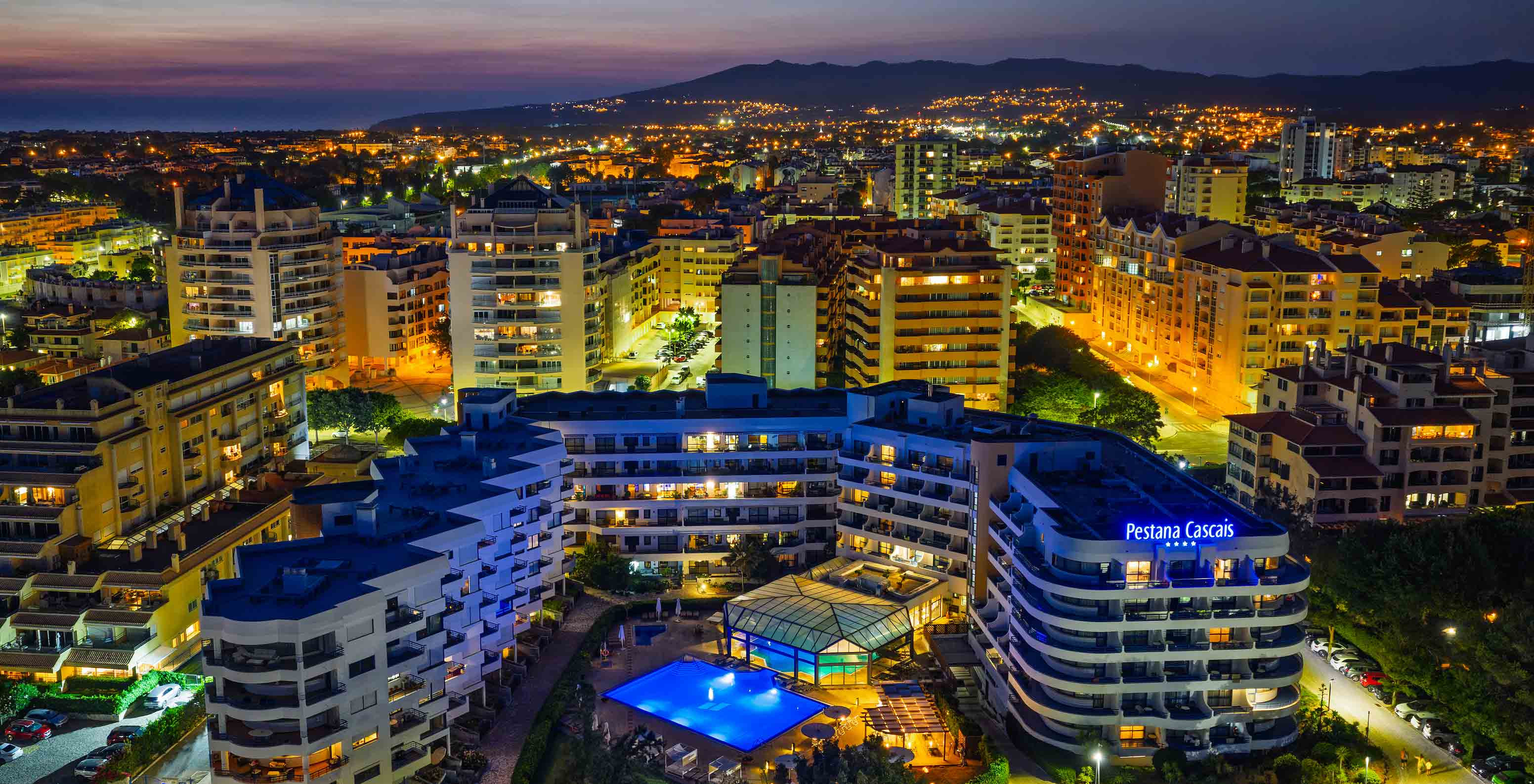 Night aerial view of Pestana Cascais and the city behind, all lit up with an orange sky