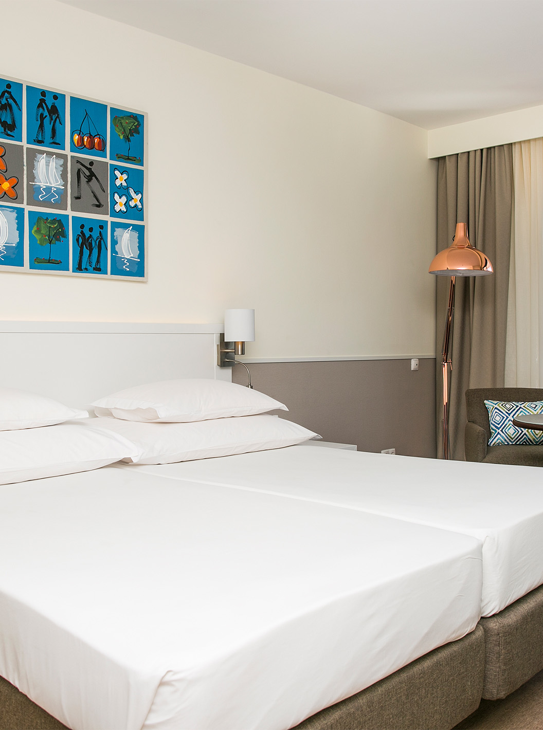The Deluxe Sea View room at Pestana Cascais has two single beds, bedside lamps, and an armchair with a table