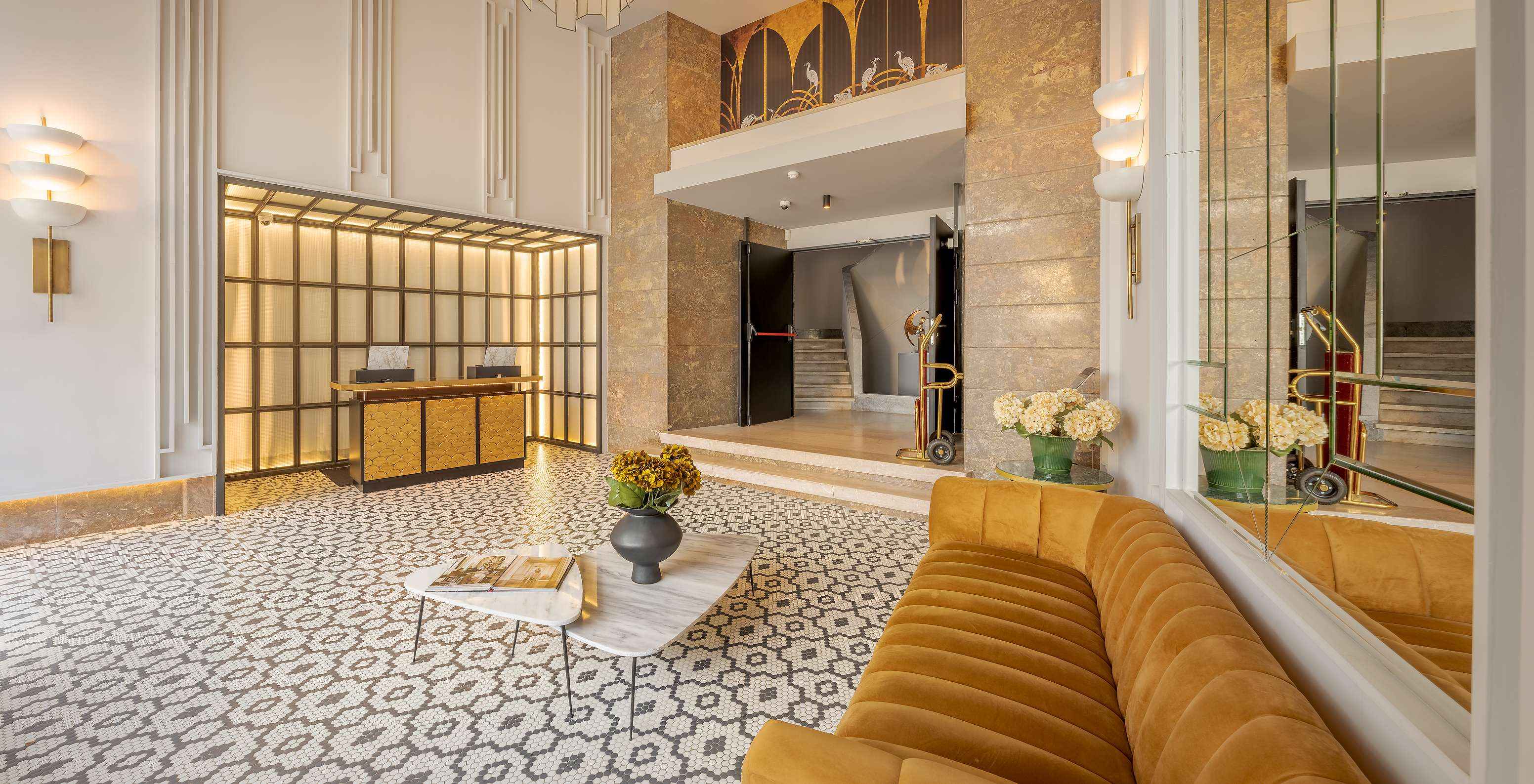 Reception lounge with a couple and child walking, mirrors, a sofa, side tables with flower pots and reception