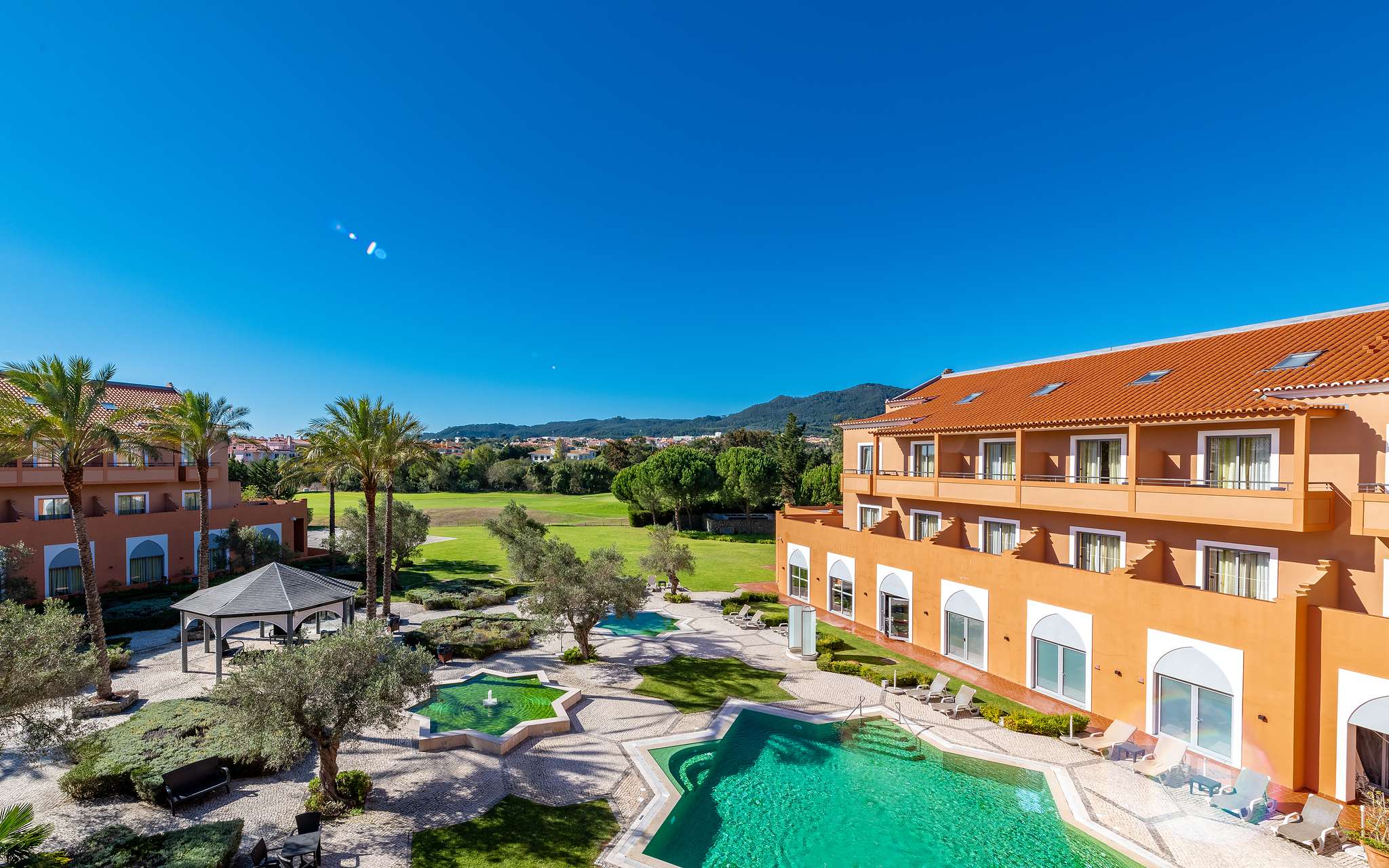 View of Pestana Sintra Golf, a 4-star hotel in Sintra, with an outdoor pool, garden with trees, and a golf course