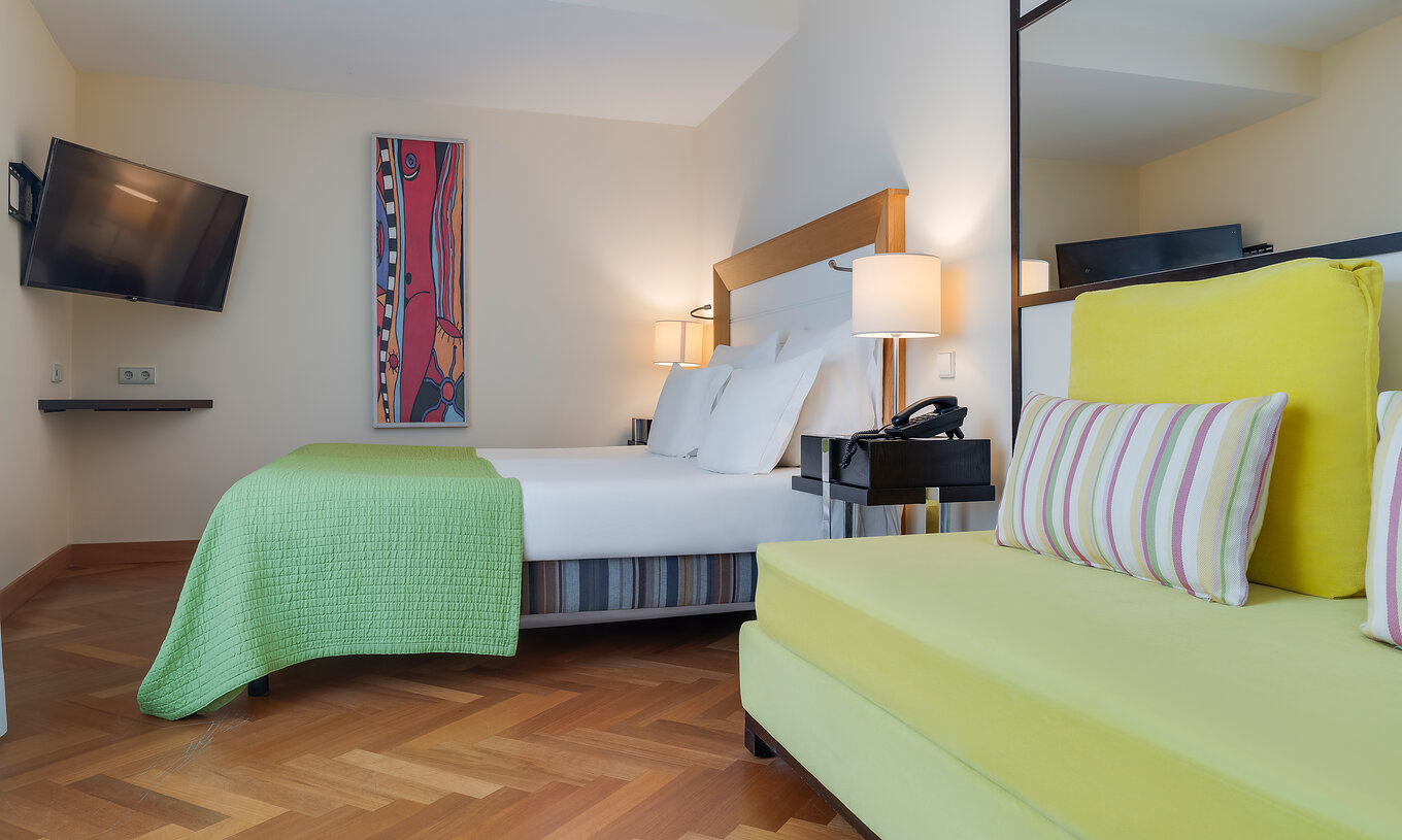 The Classic Twin of Pestana Promenade has a double bed with a green bedspread and a mounted television