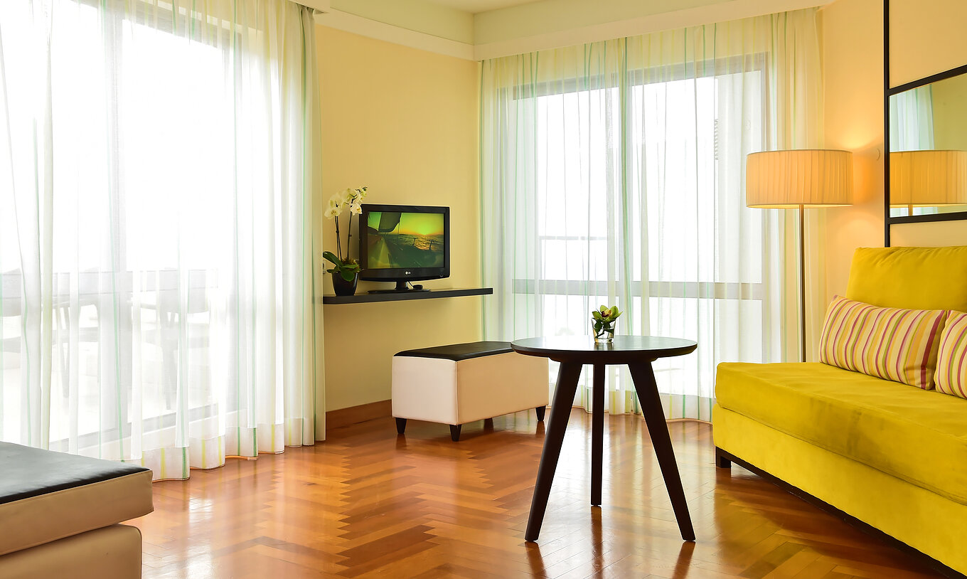 The Junior Suite of Pestana Promenade has a living room with a green sofa, a television, and two large windows