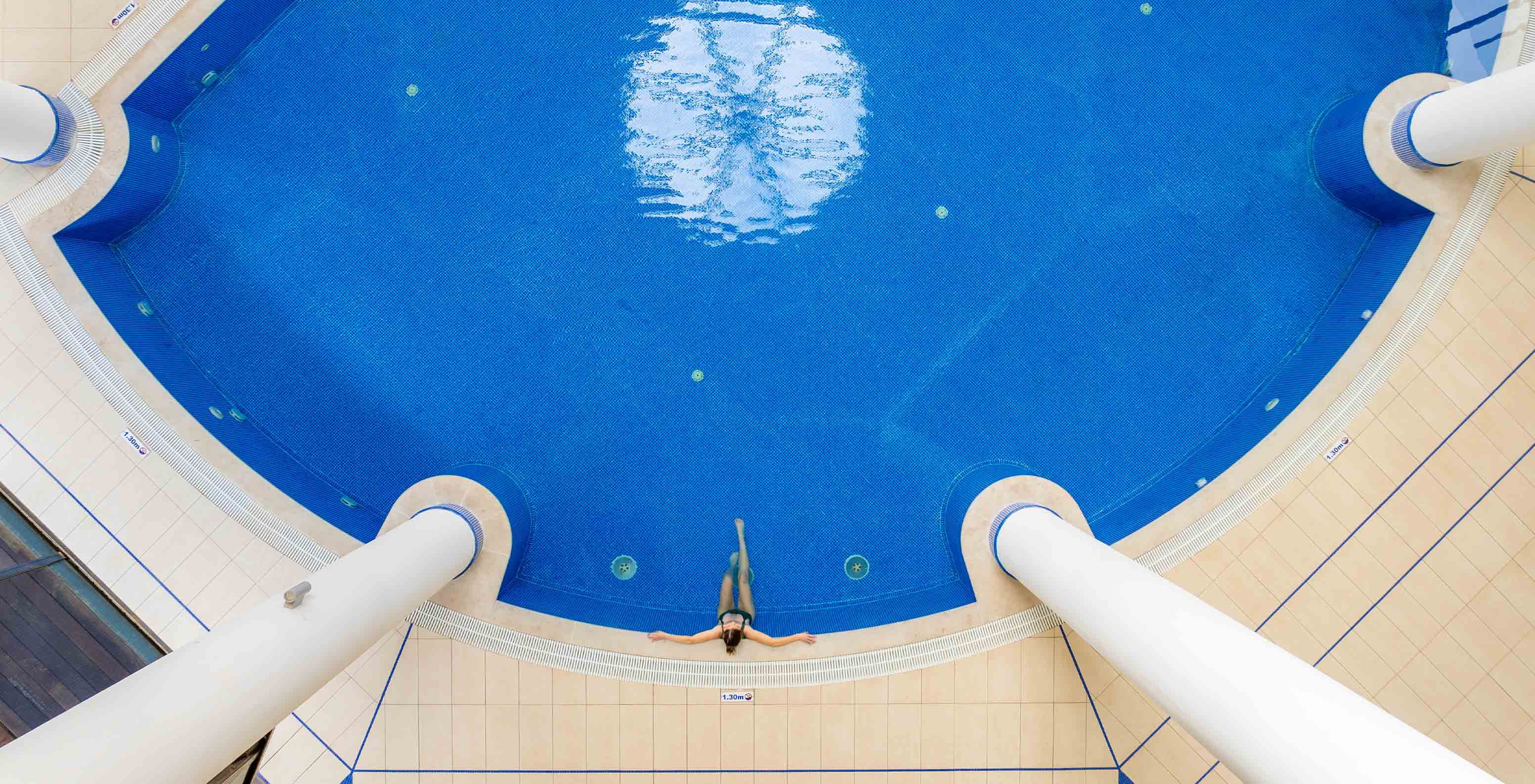 View of the blue indoor pool at Pestana Porto Santo, with a guest in the water