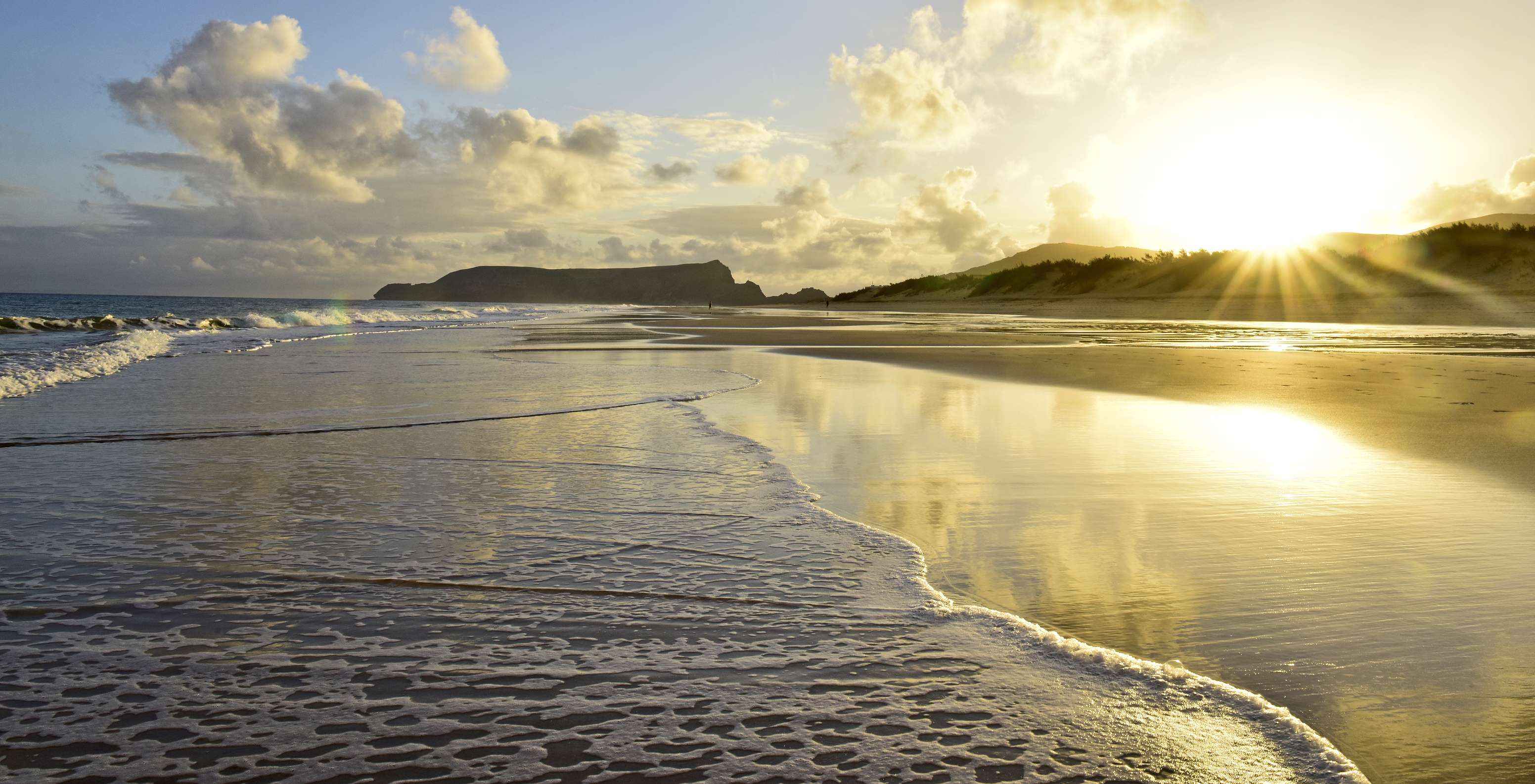 Sunset on Porto Santo beach, with an orange cloud-filled sky and the sun casting golden rays over the sea