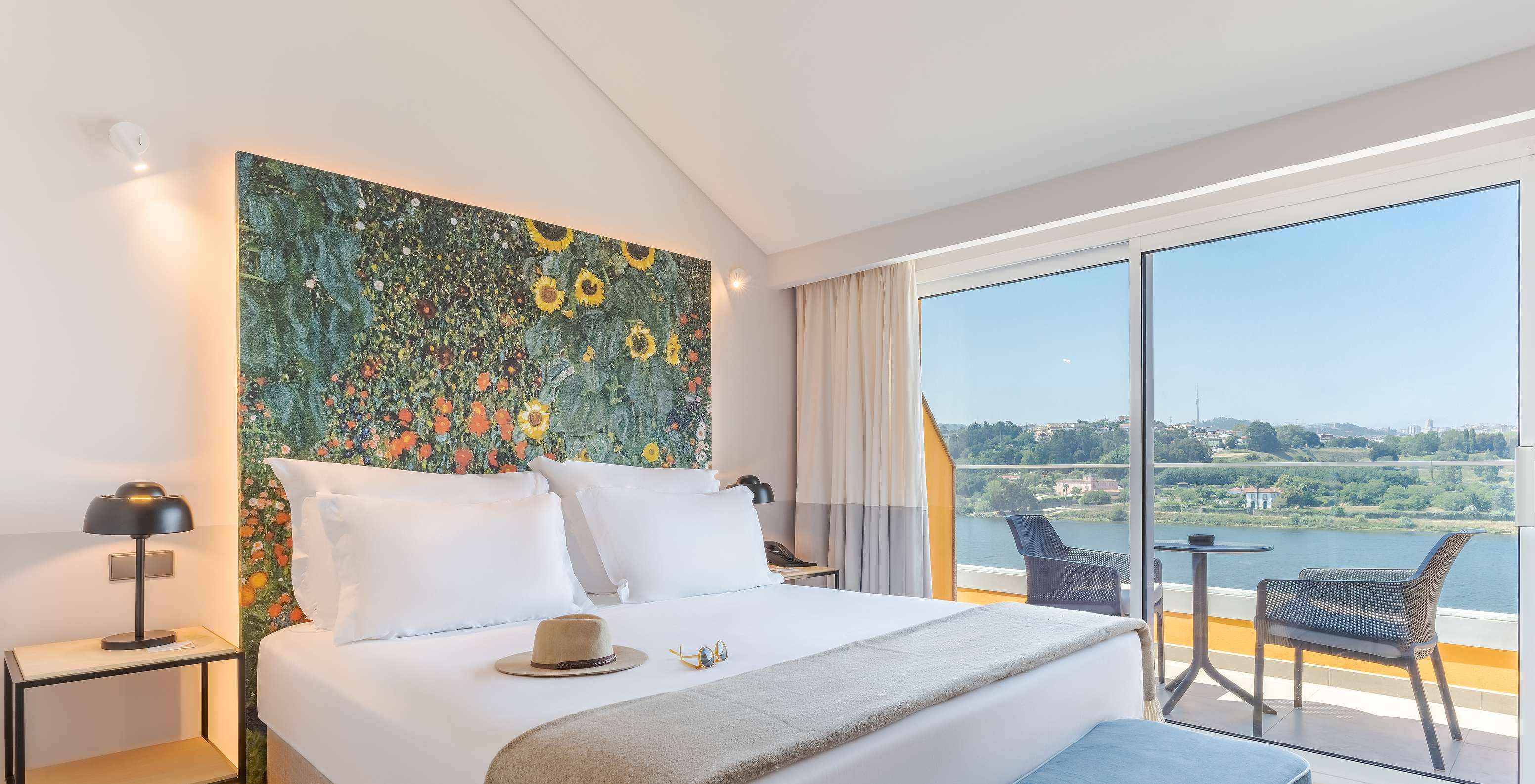 The Junior Suite at Pestana Douro Riverside includes a double bed, bedside table with a lamp, and a balcony with a view