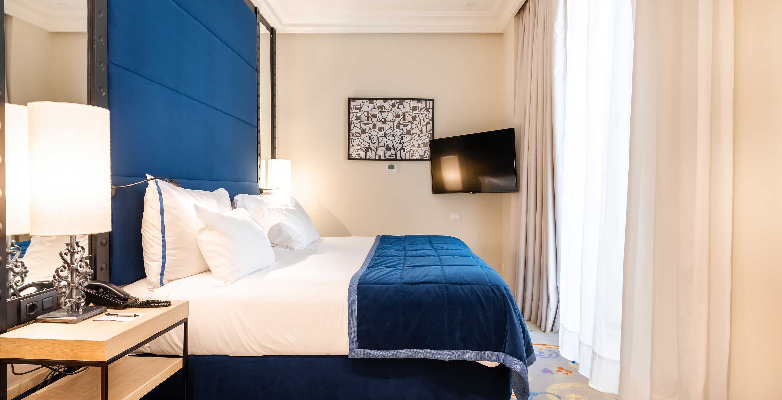The Superior room at Pestana Collection Plaza Mayor has a double bed, a blue headboard, a television and mirrors