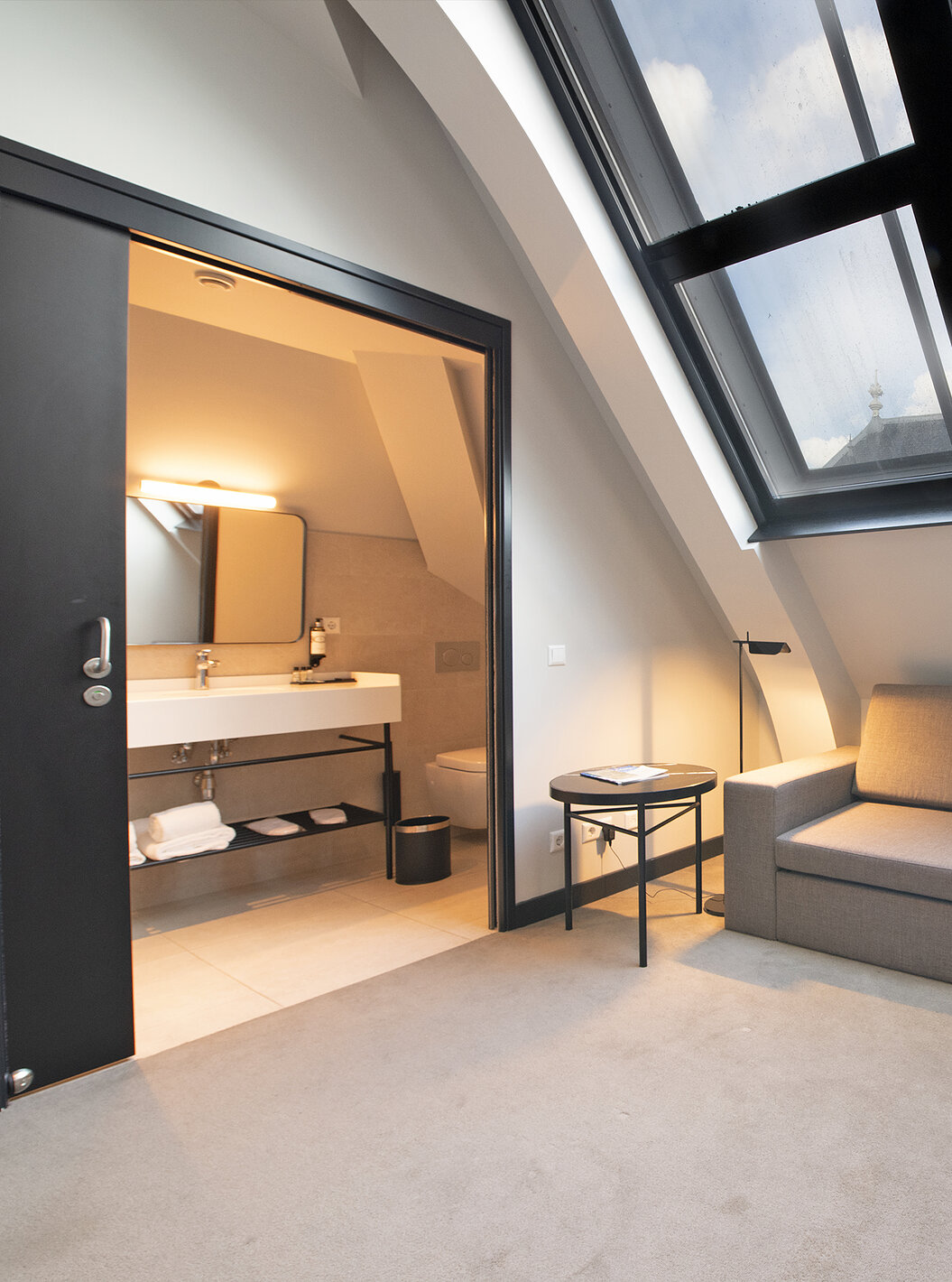 Loft room at Pestana Amsterdam Riverside has a gray sofa, and a bathroom with sink and mirror