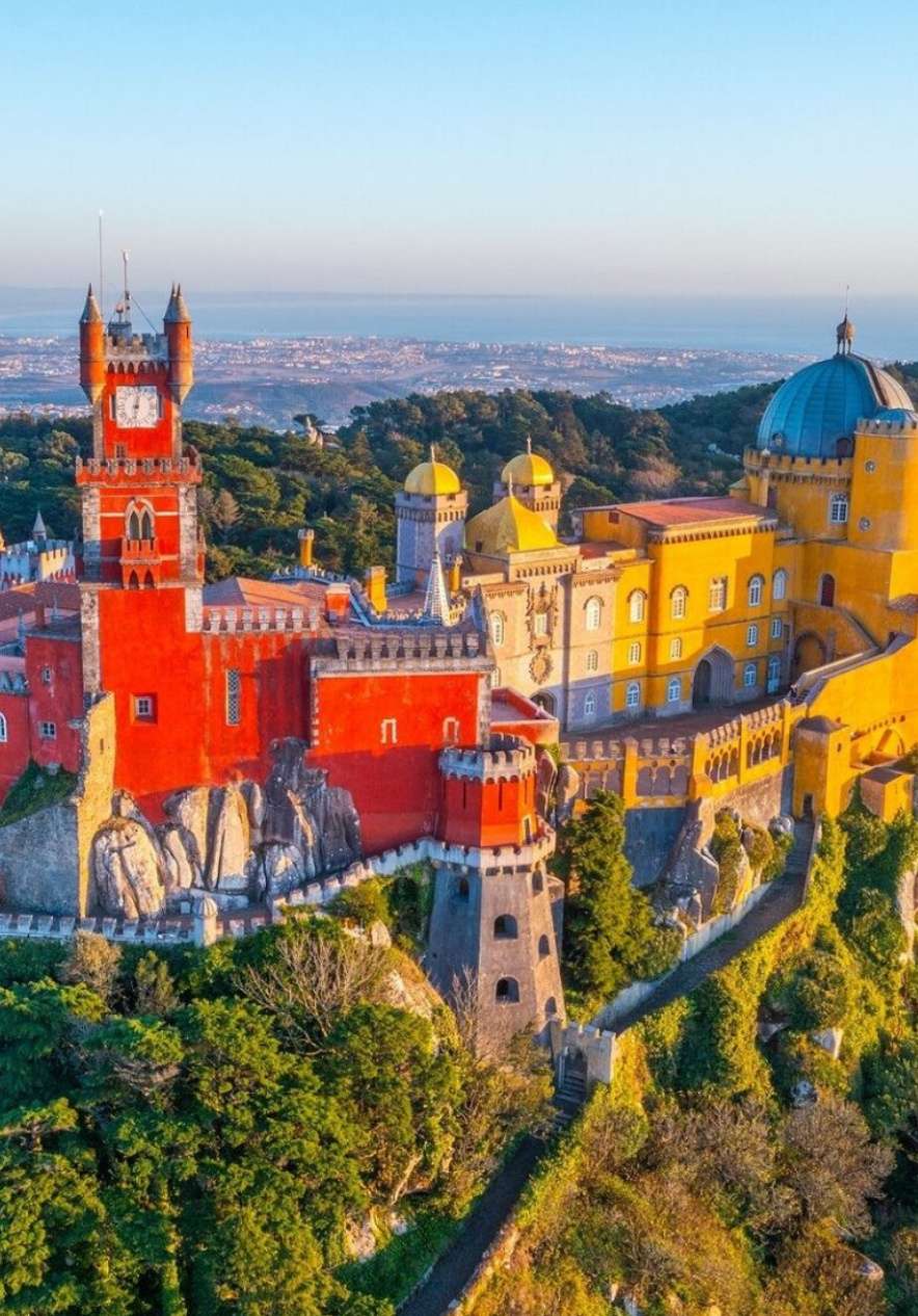Panoramic view of the Pena Palace in Sintra, with its red and yellow-toned facades and the sea in the background