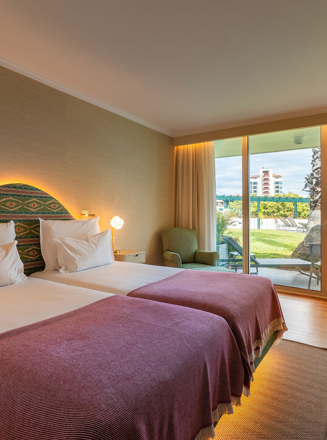 The Pool View Room at Pestana Quinta Perestrello has a double bed with a pink bedspread and a balcony with a view.
