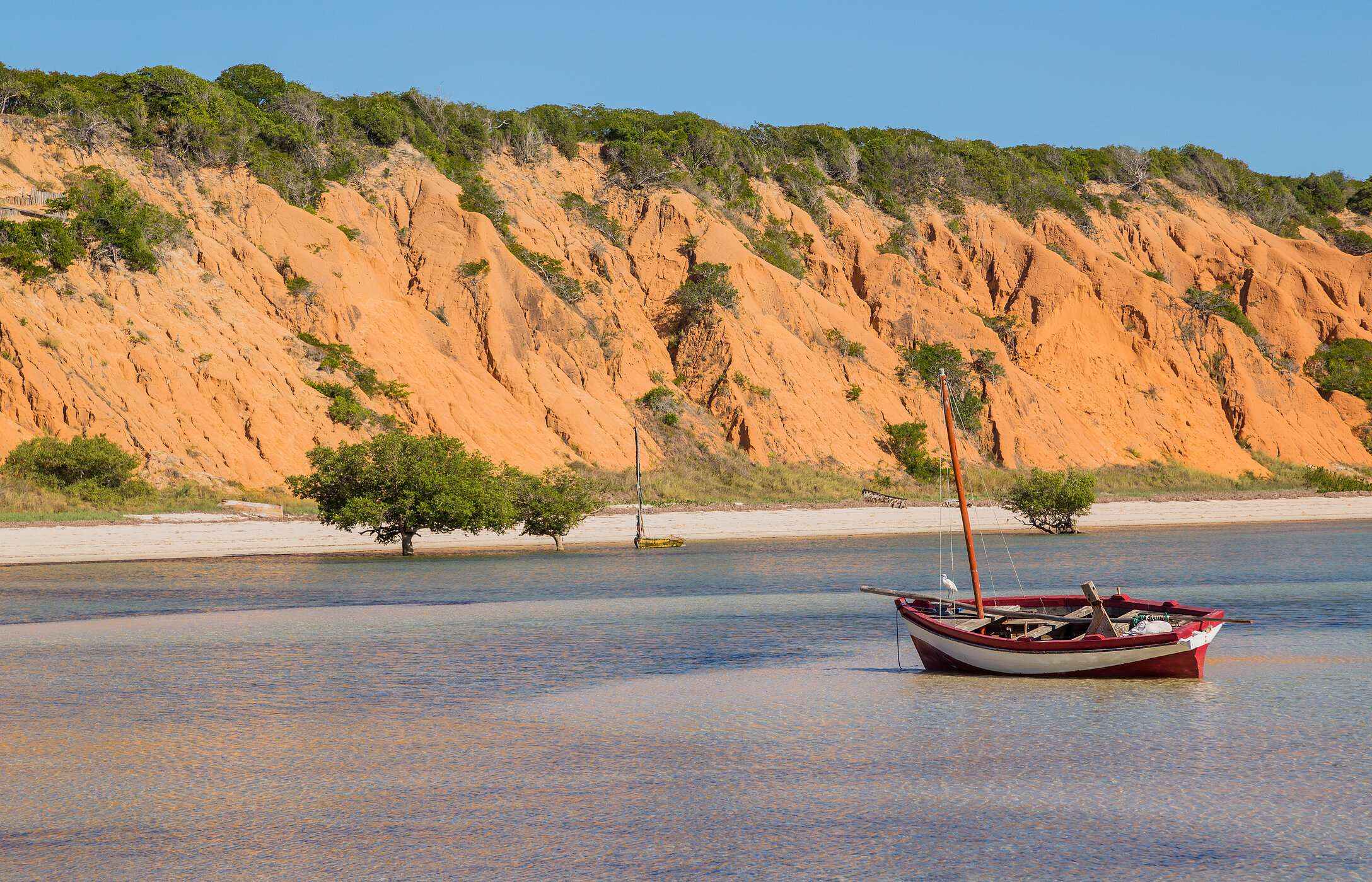 Vista del mar desde la isla de Magaruque con un barco tradicional anclado y acantilados rojizos al fondo
