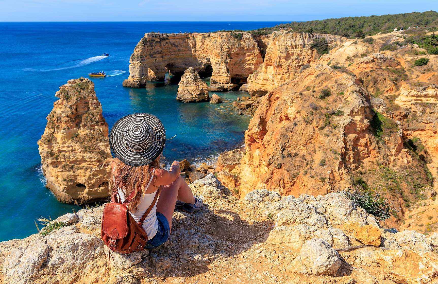 Mujer admirando la vista panorámica de la costa del Algarve, con aguas cristalinas y un acantilado rodeado de vegetación