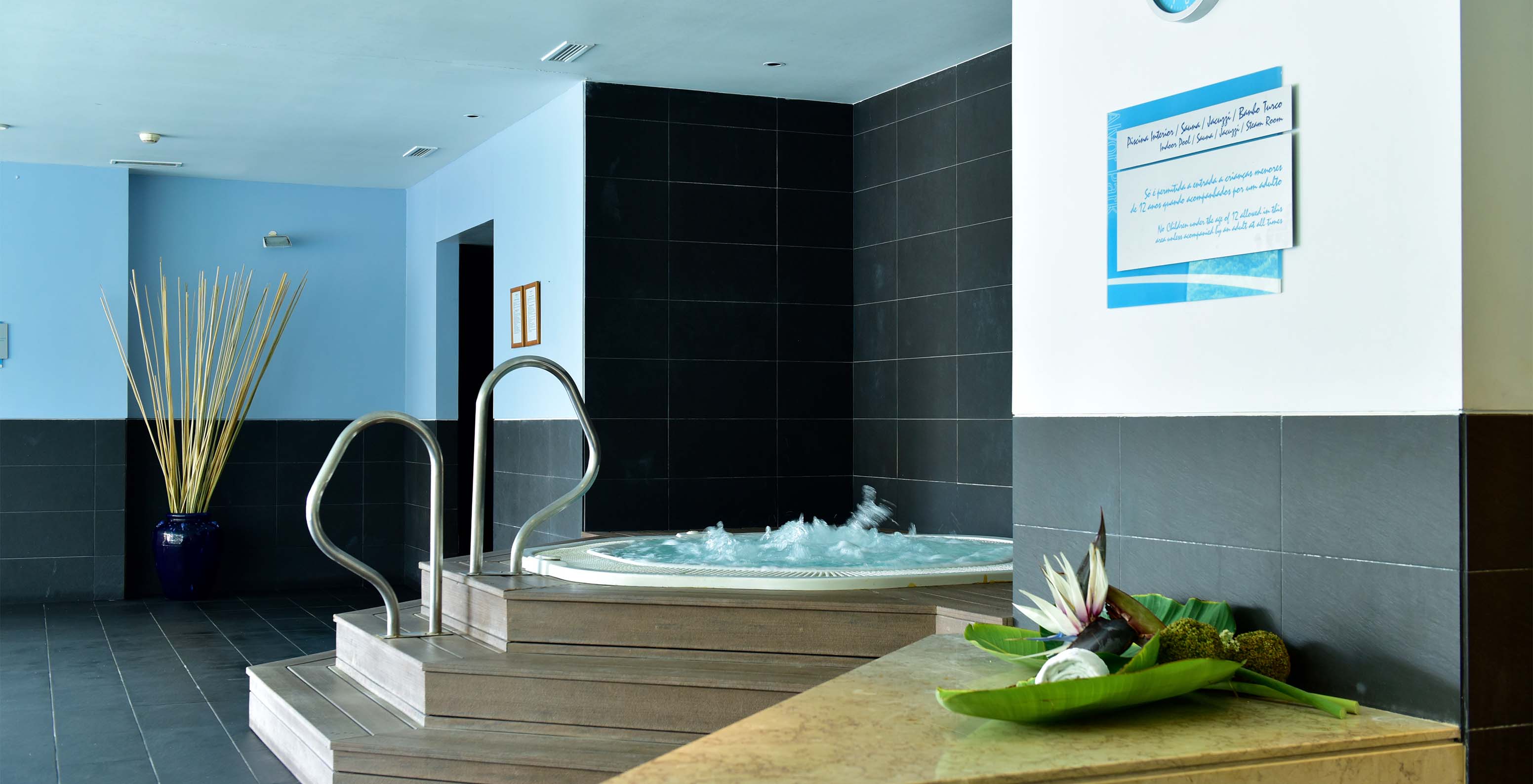 Jacuzzi con escaleras de madera y apoyos metálicos, con suelo de piedra negra y reloj de pared