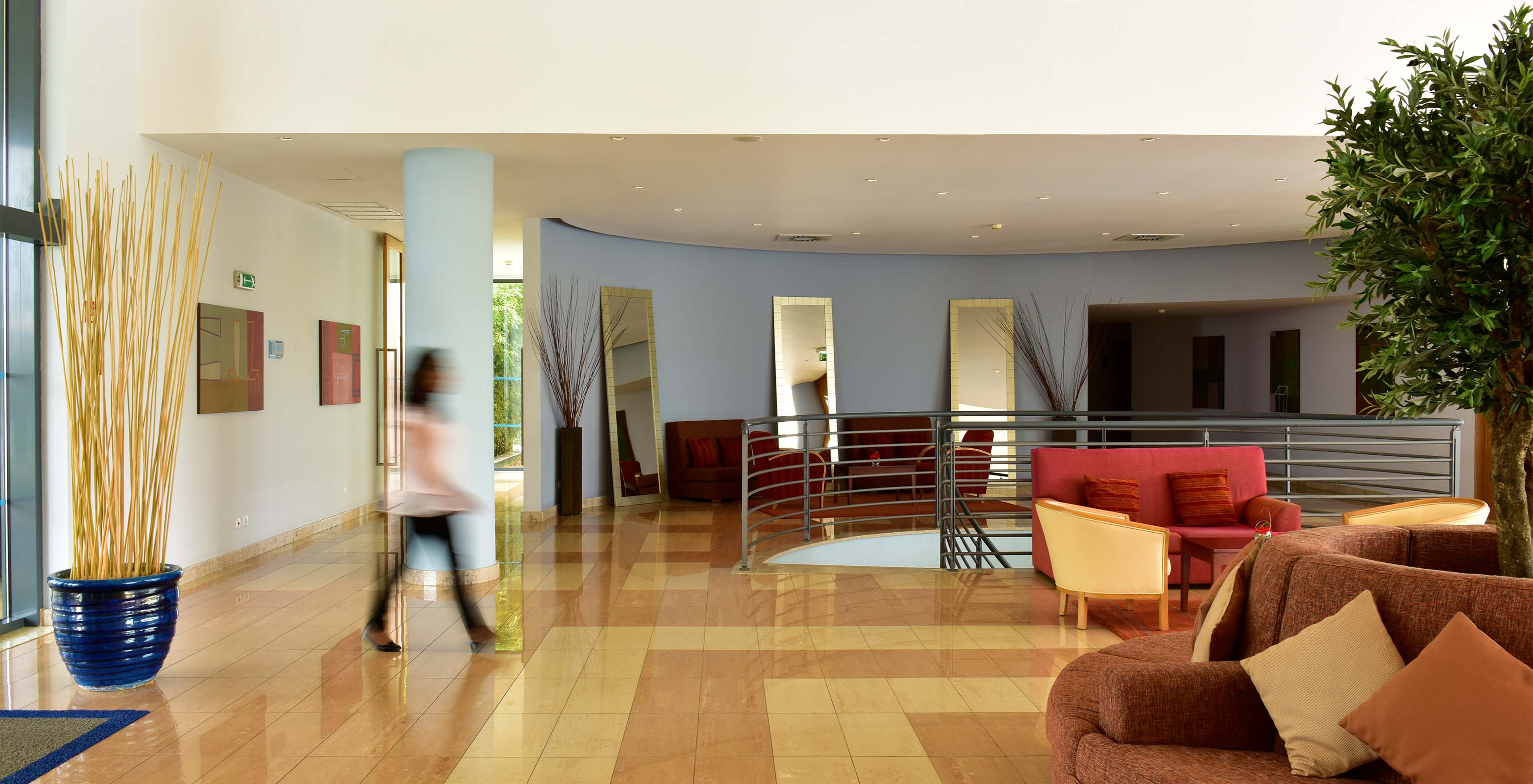 Entrada del hotel con sofás rojos y naranjas, con escaleras metálicas y una mujer caminando