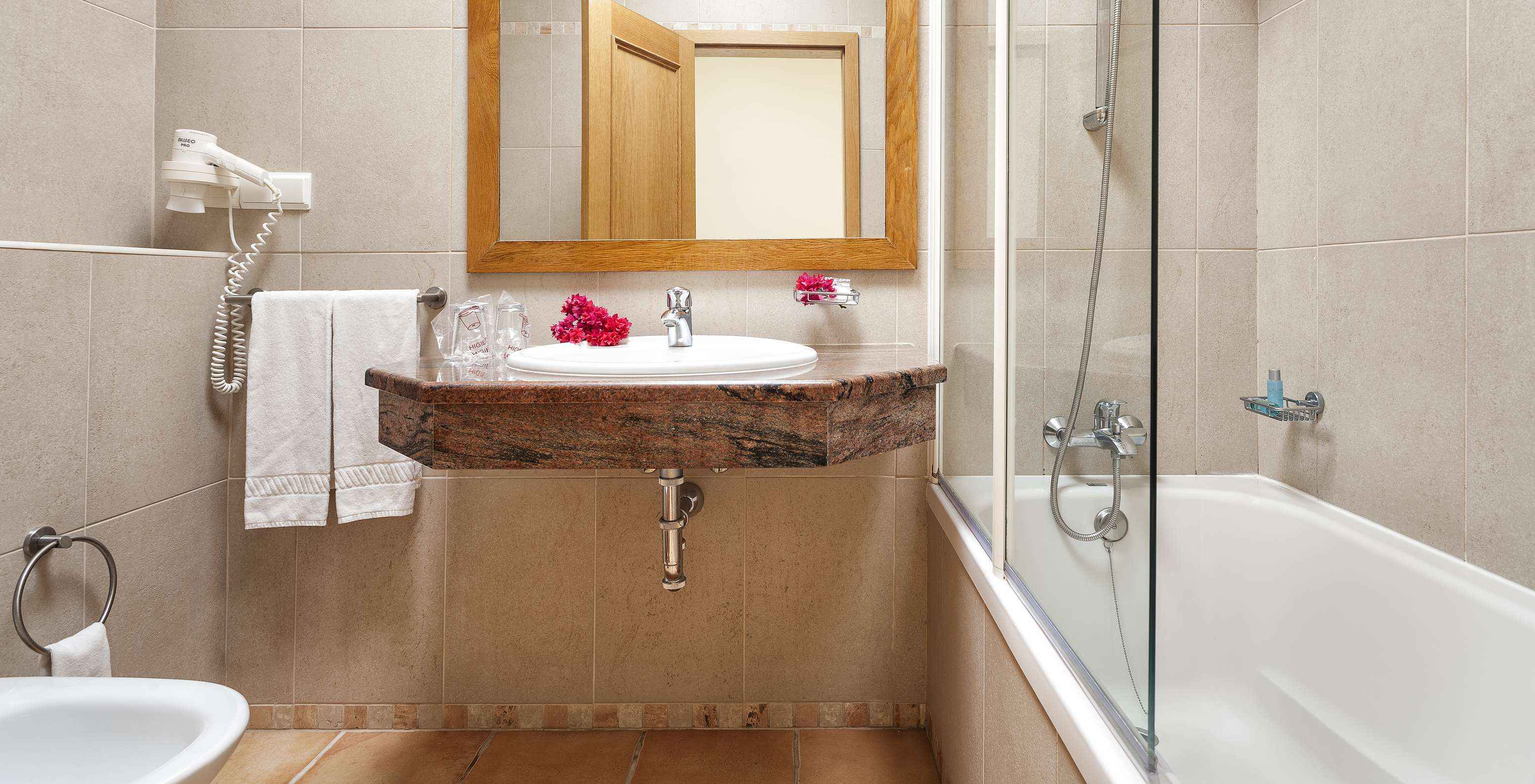 El Apartamento T1 - Terra del Pestana Palm Gardens tiene una bañera con ducha, un lavabo con flores y un espejo
