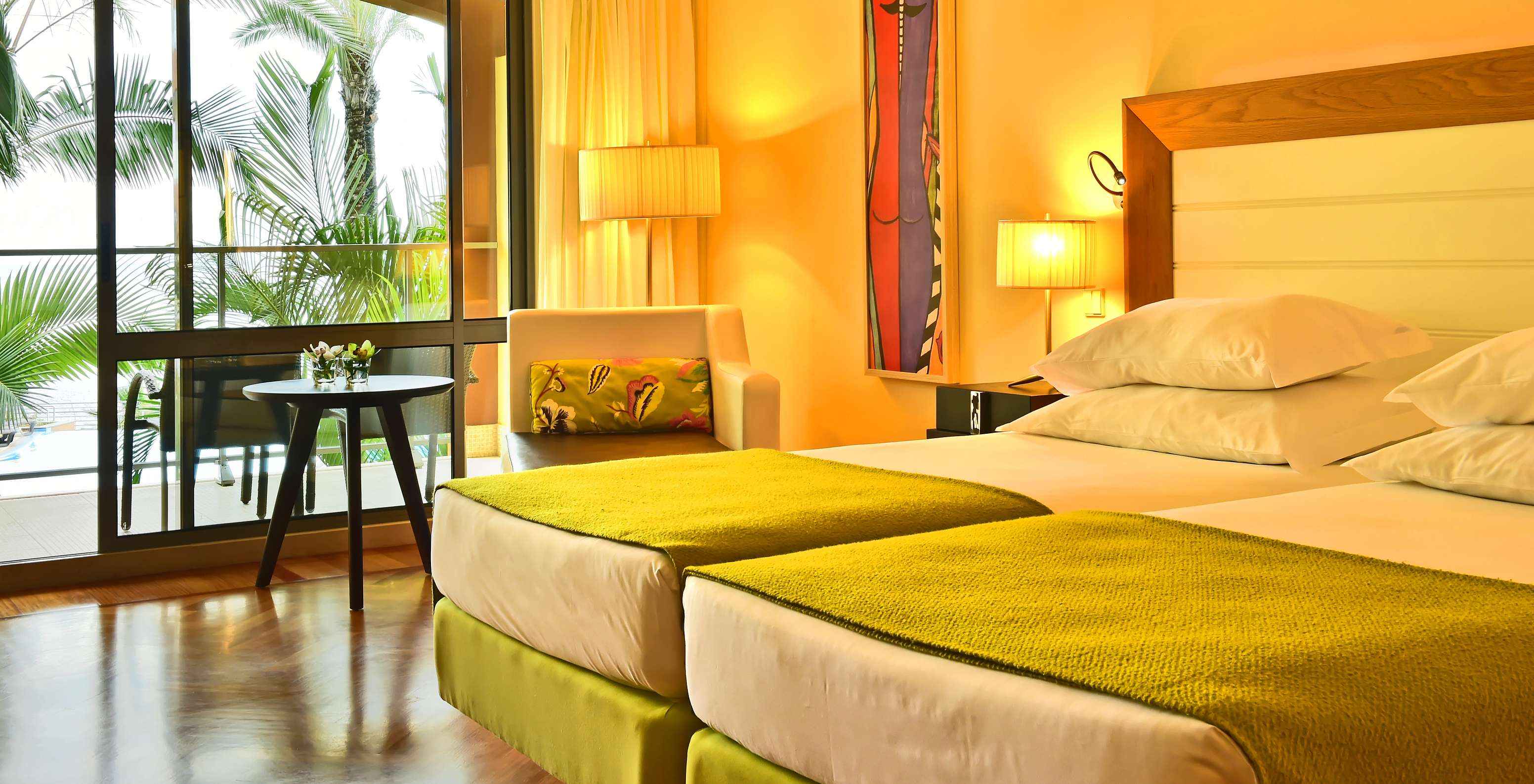 El Clásico Vista Piscina del Pestana Promenade tiene dos camas con un edredón verde y una ventana grande al balcón