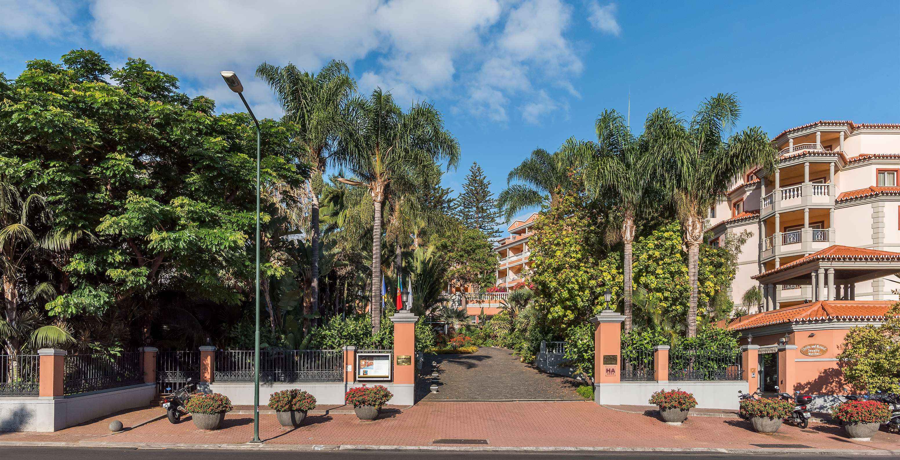 Entrada del Pestana Village, un Hotel Romántico en Funchal, en Madeira, con varias palmeras y edificios naranjas