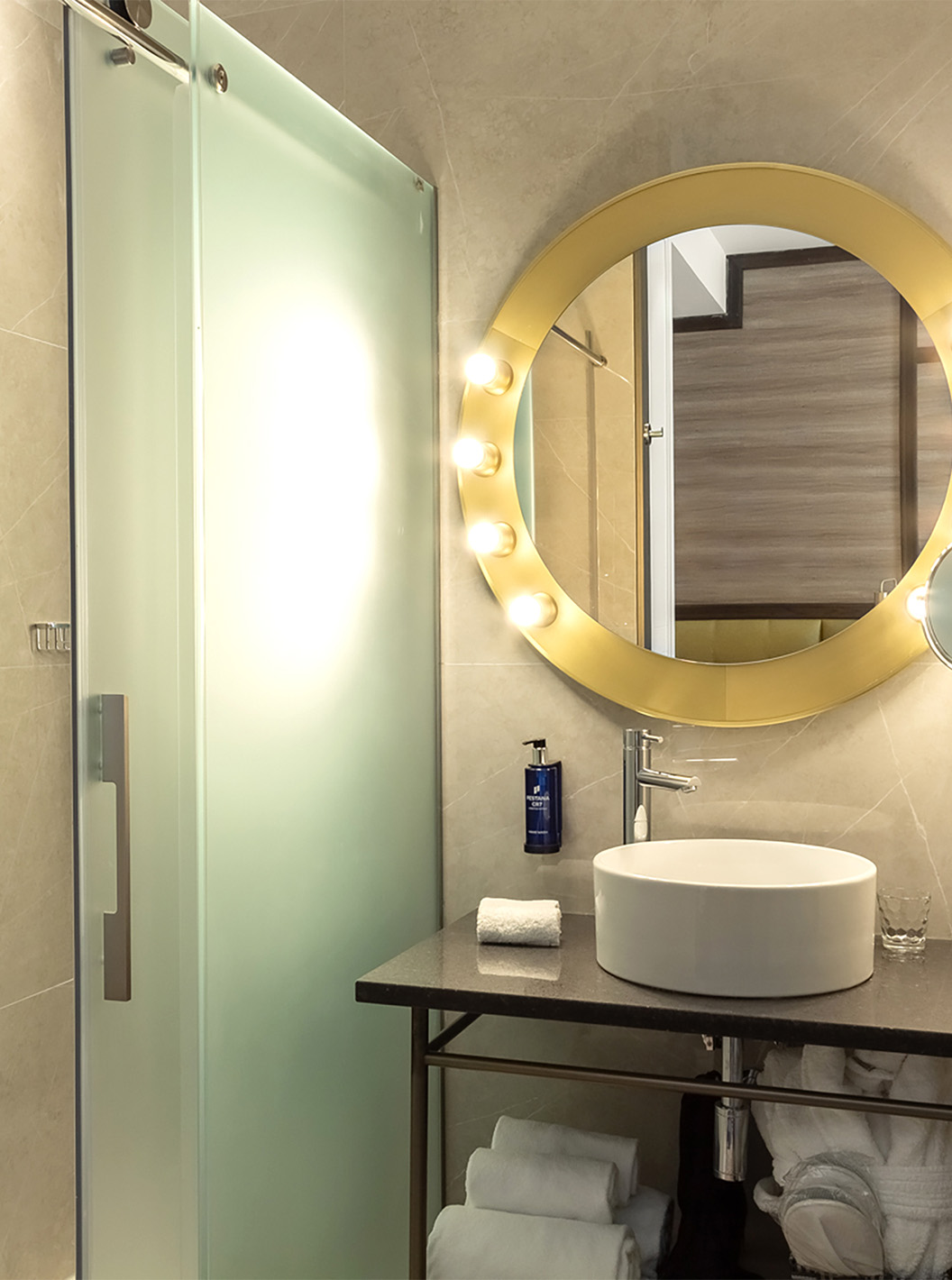 El Premium del Pestana CR7 Gran Vía Madrid tiene un baño con un espejo y luces, lavabo y puertas de vidrio corredizas