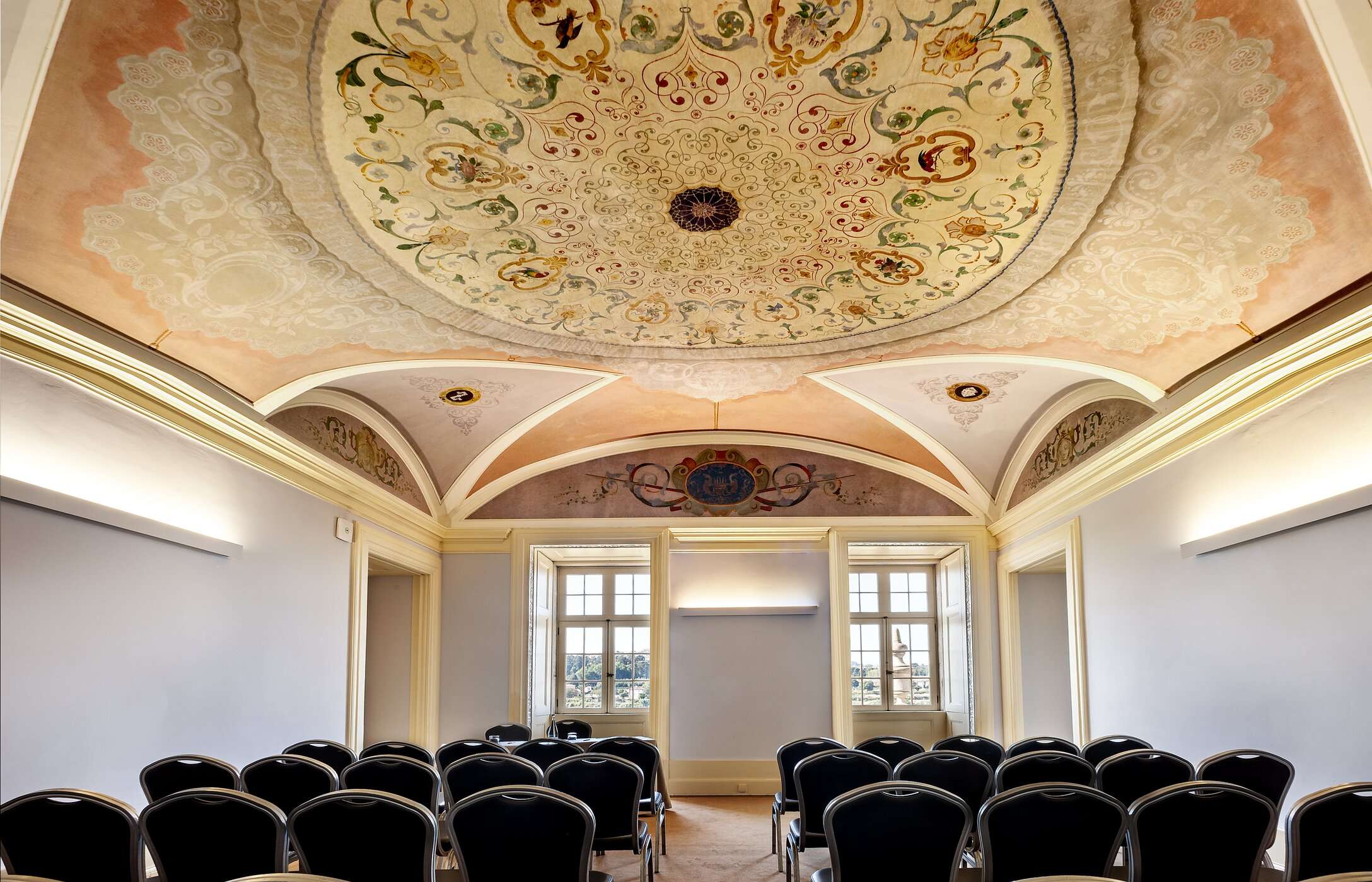Sala para reuniones o conferencias, con techo con detalles y adornos, sillas y grandes ventanas que permiten la luz natural