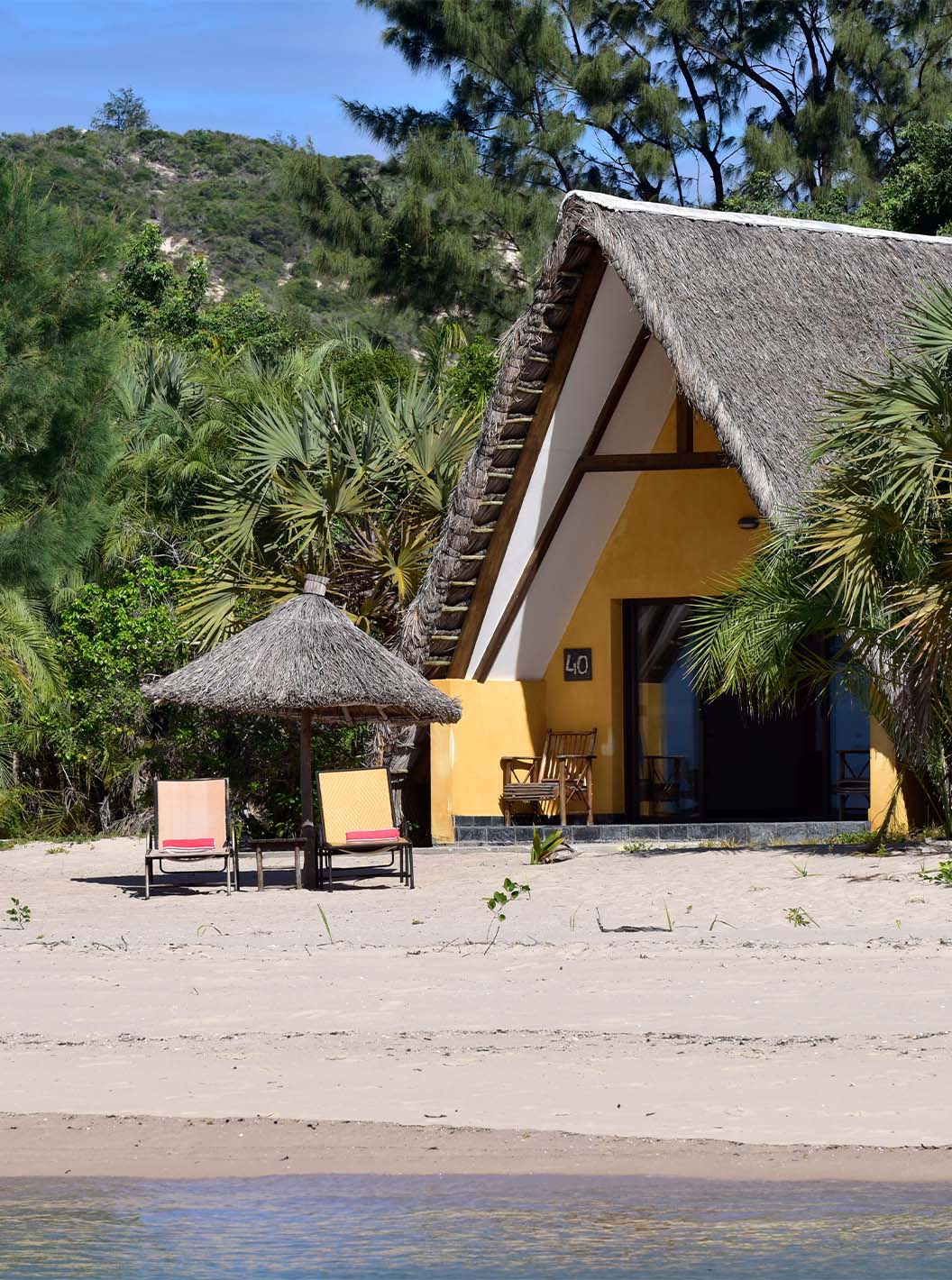 Bungalow Suite T2 van Pestana Bazaruto Lodge is een huisje met rieten dak op het strand en omgeven door groene natuur