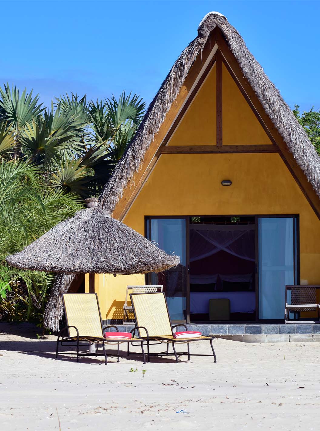 Bungalow T1 van Pestana Bazaruto Lodge is een geel huisje op het strand met rieten dak en A-vorm