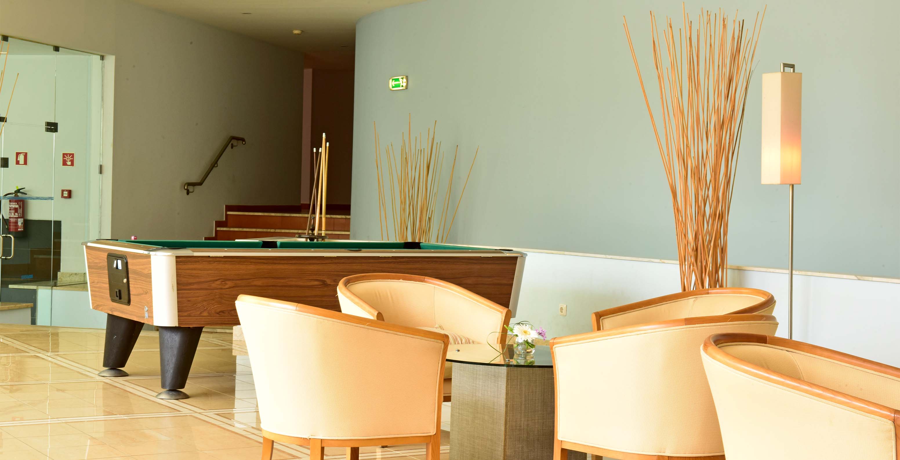 Spelletjeskamer met biljarttafel, stoelen en centrale bijzettafel, met trappen op de achtergrond en decoratie