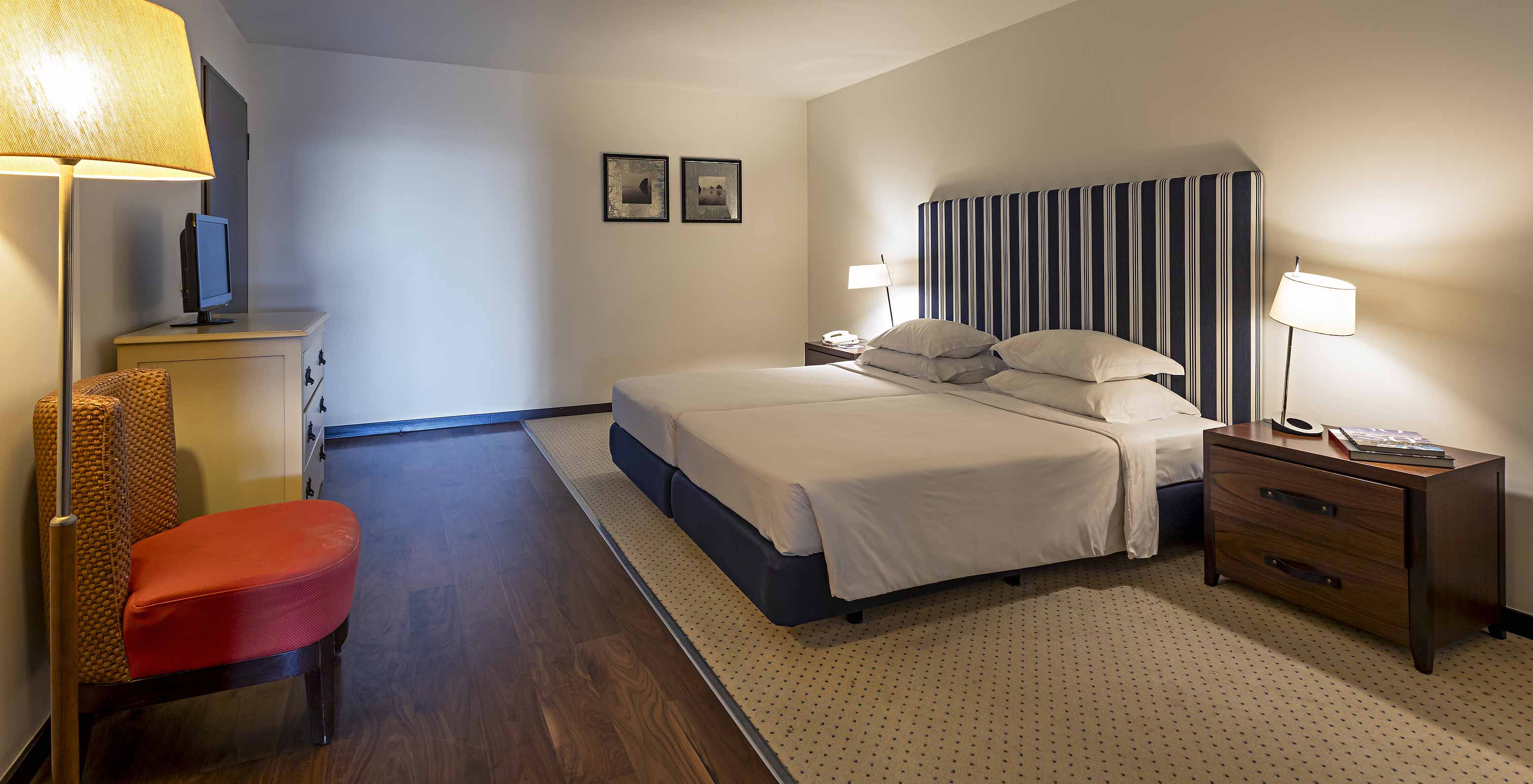 De Cliff Suite T2 in Pestana Alvor Praia heeft een grote kamer met tweepersoonsbed, twee schilderijen en een dressoir met tv