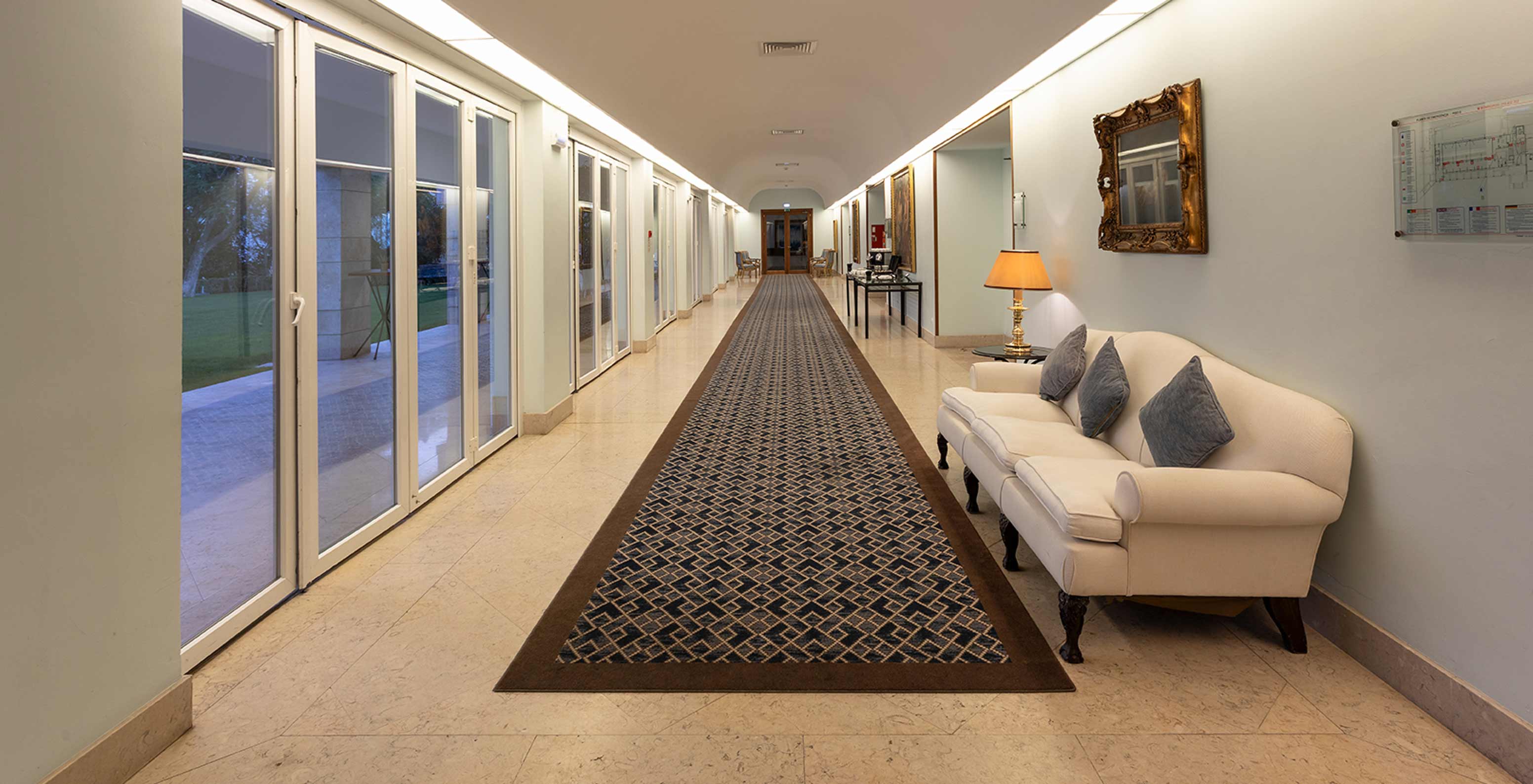 Pestana Palace Lisboa heeft een foyer met lang blauw tapijt, een bank en grote ramen met lange gordijnen