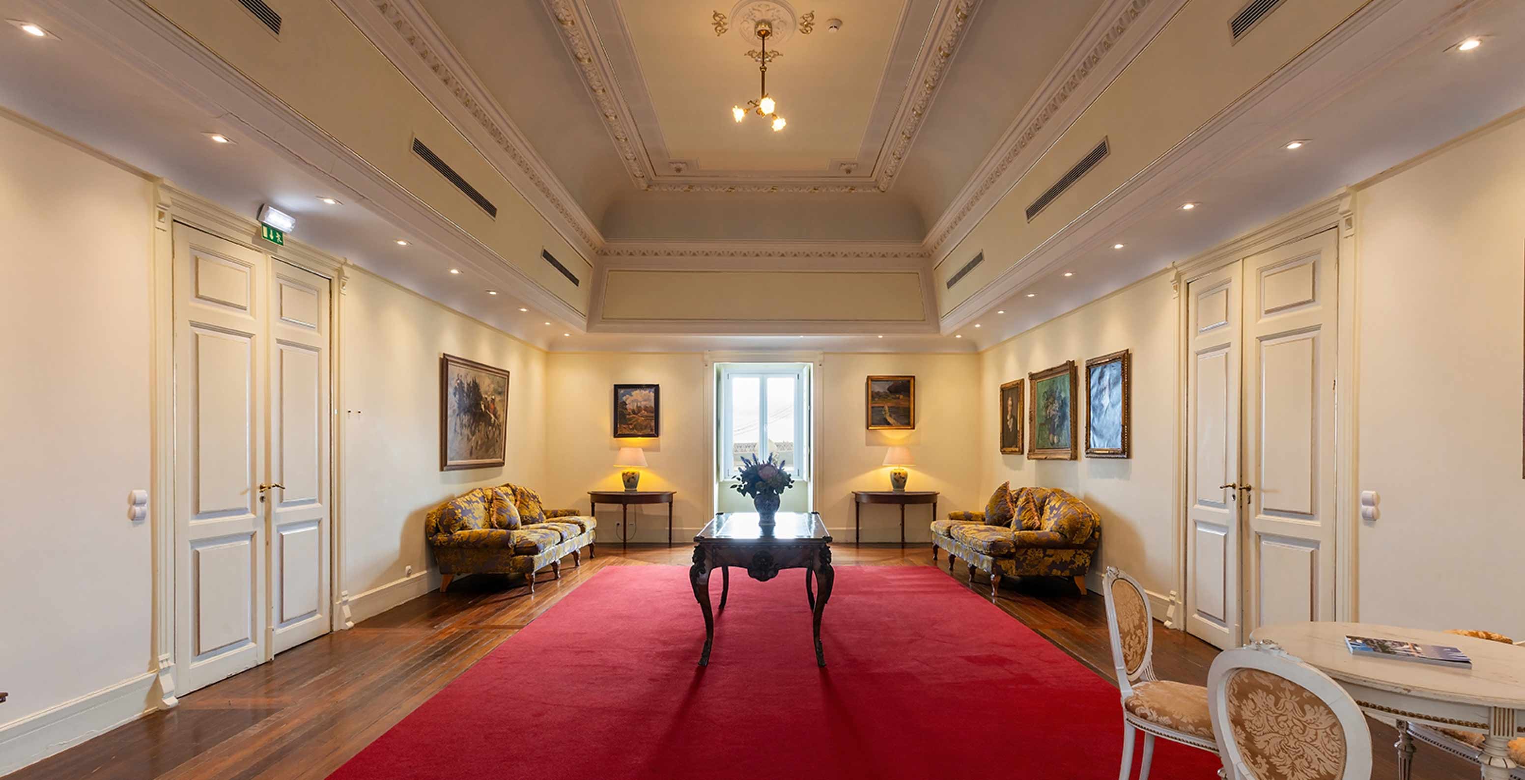 Pestana Palace Lisboa heeft een foyer met groot rood tapijt, twee banken en een raam in de hoek	