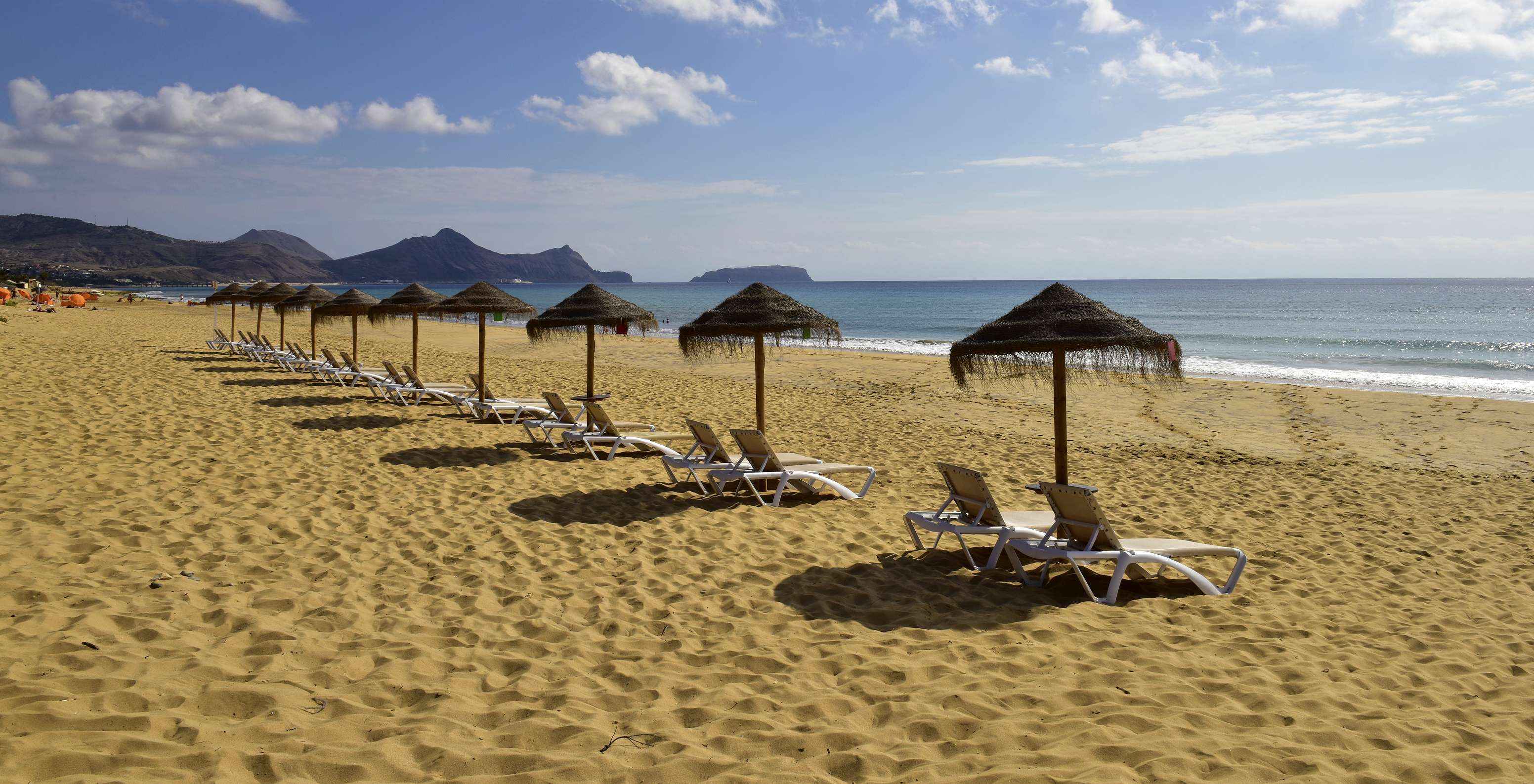 Strand met fijn zand, blauw water en bergen op de achtergrond van Pestana Porto Santo, hotel met alles-inclusief en spa