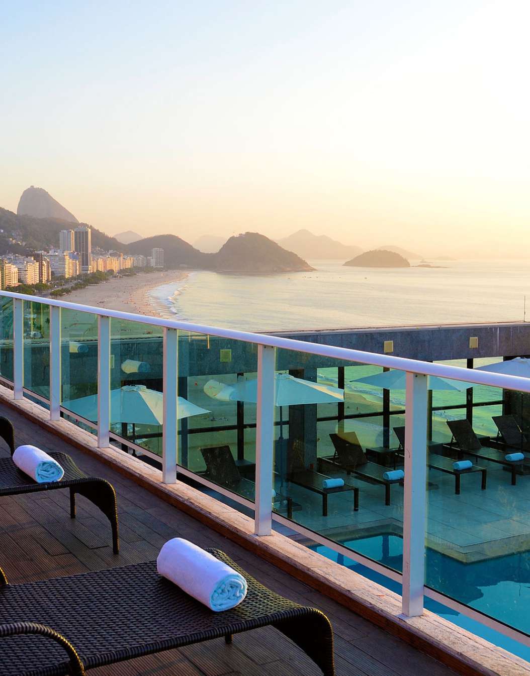 Rooftop do hotel 4 estrelas no Rio de Janeiro, com espreguiçadeiras com toalhas e vista para a Praia de Copacabana