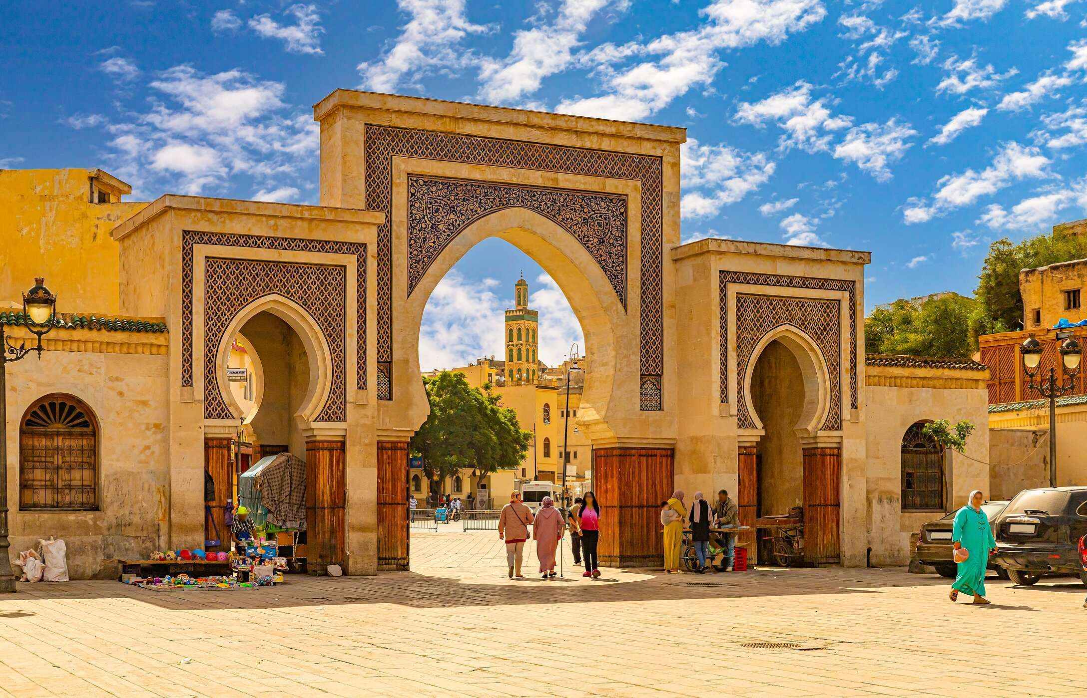 Arcos típicos de Marrocos, na cidade de Fez, com azulejos e cor de areia, e pessoas a passear com roupas tradicionais