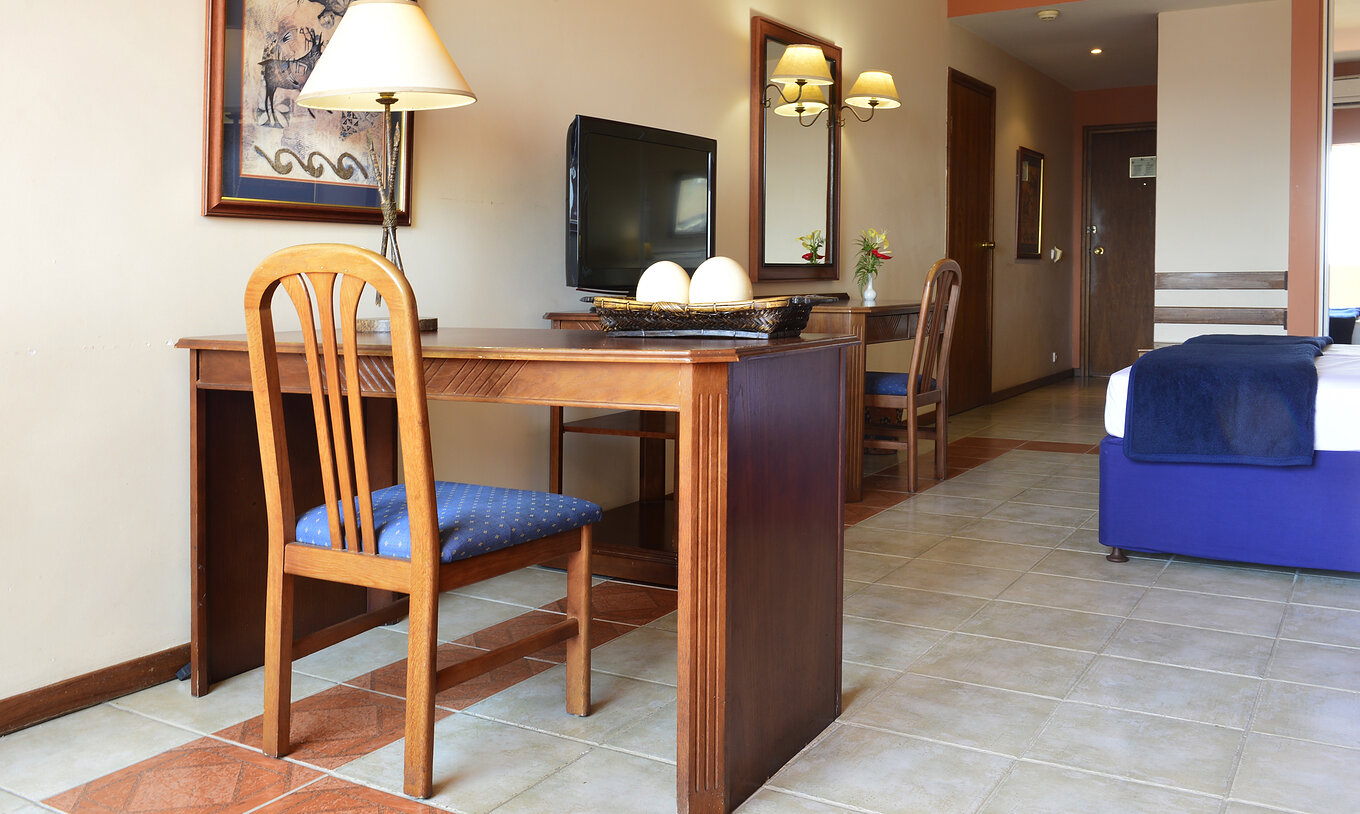 A Suite Executiva Familiar do Pestana Rovuma tem uma secretária e uma cadeira de madeira, com um candeeiro e um quadro