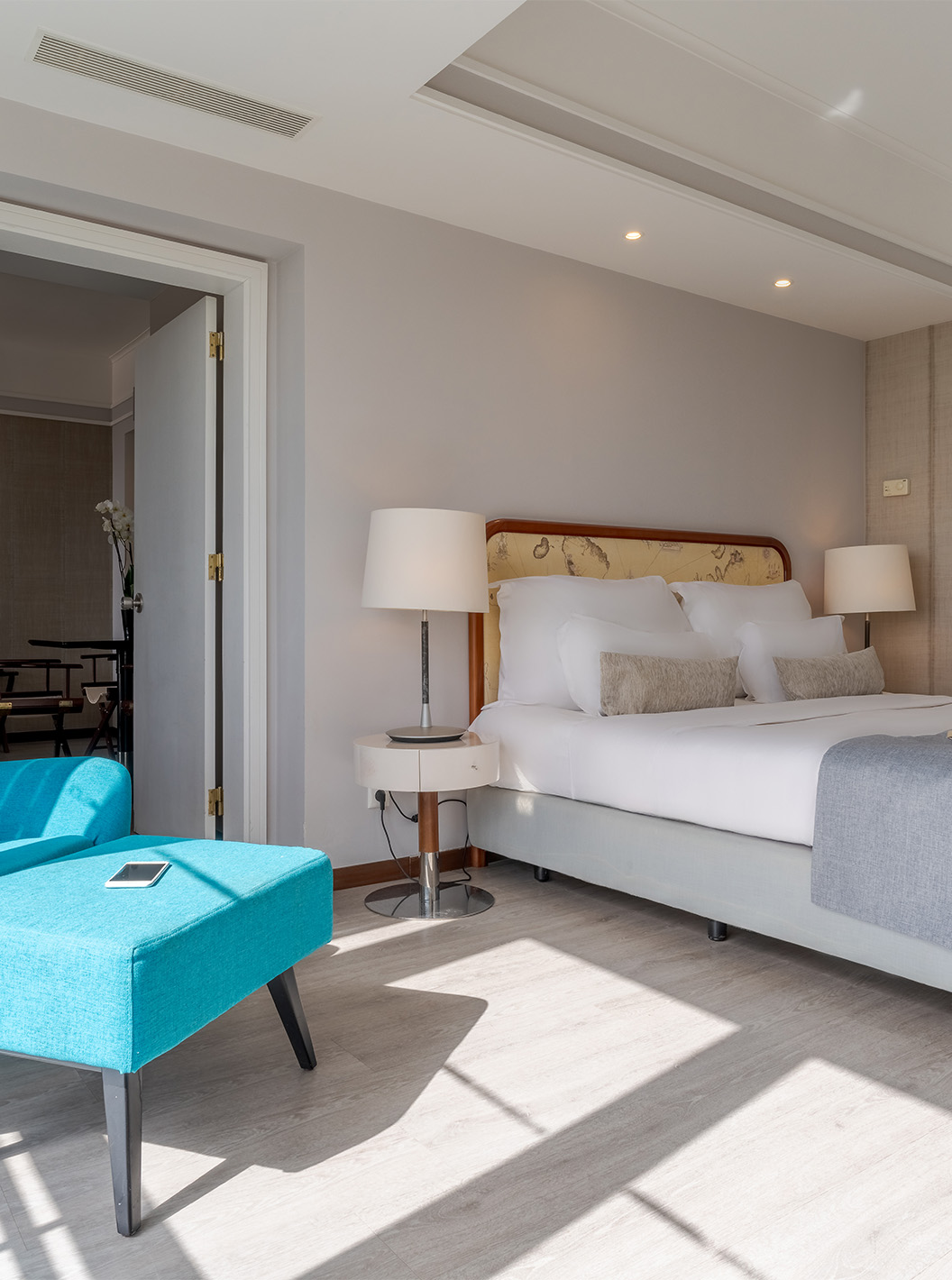 A Suite Vista Mar do Pestana Alvor Praia tem cama de casal com cadeirão e pousa-pés azuis, com candeeiros e chão de madeira