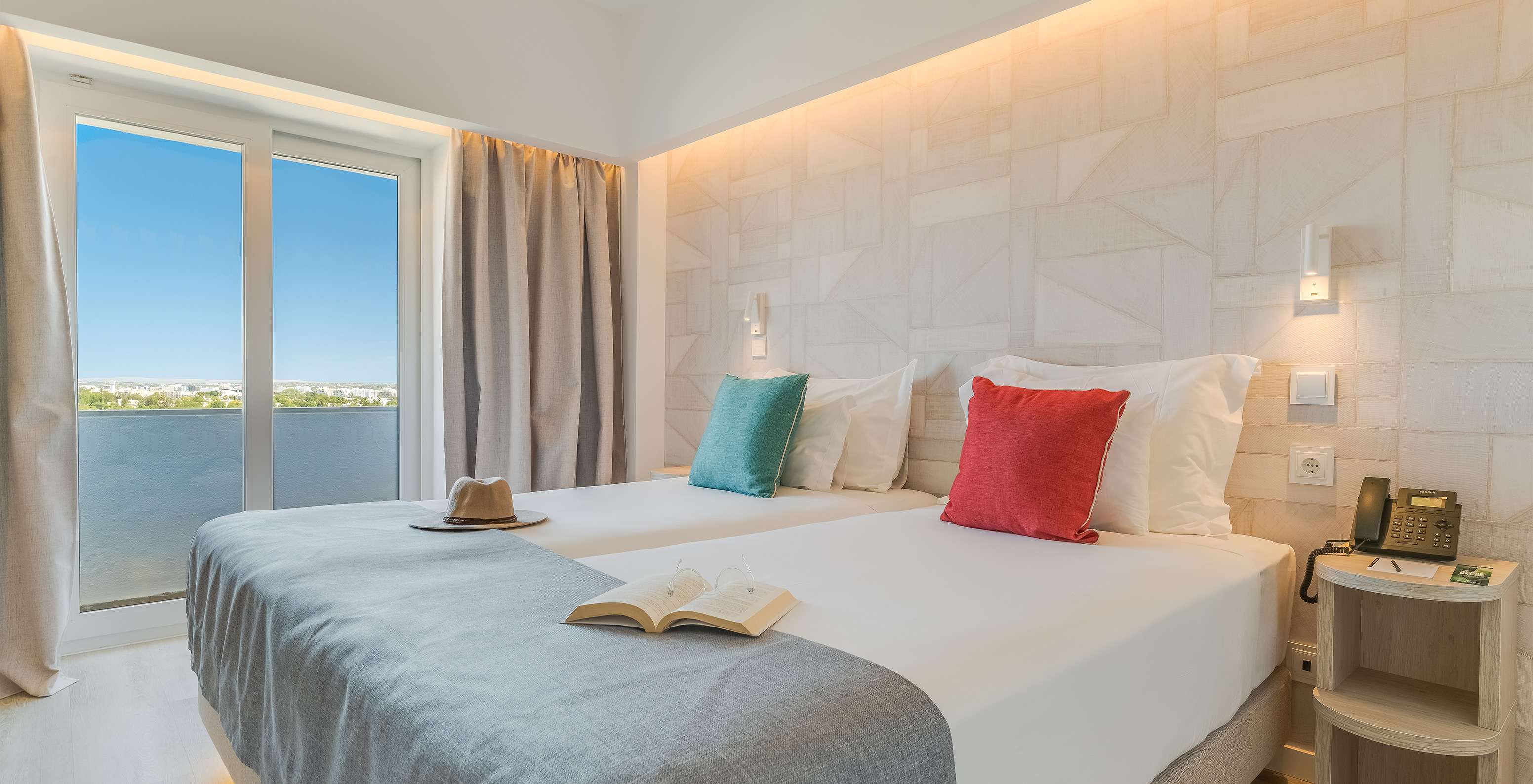 O Quarto Clássico Vista Jardim do Pestana Blue Alvor Beach tem duas camas com lençóis brancos e almofadas coloridas