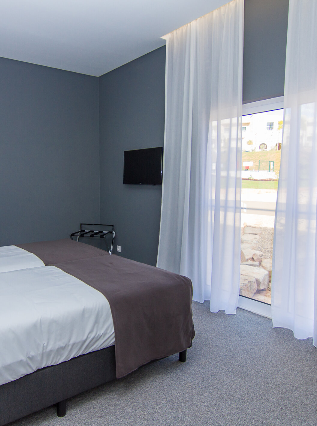 O Quarto Clássico do Pestana Gramacho Residences tem duas camas individuais, uma televisão e uma janela com cortinas