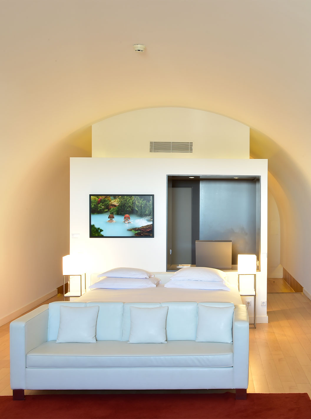 A Junior Suite Art District do Pestana Cidadela Cascais tem uma cama de casal com sofá branco no fundo e um quadro na parede