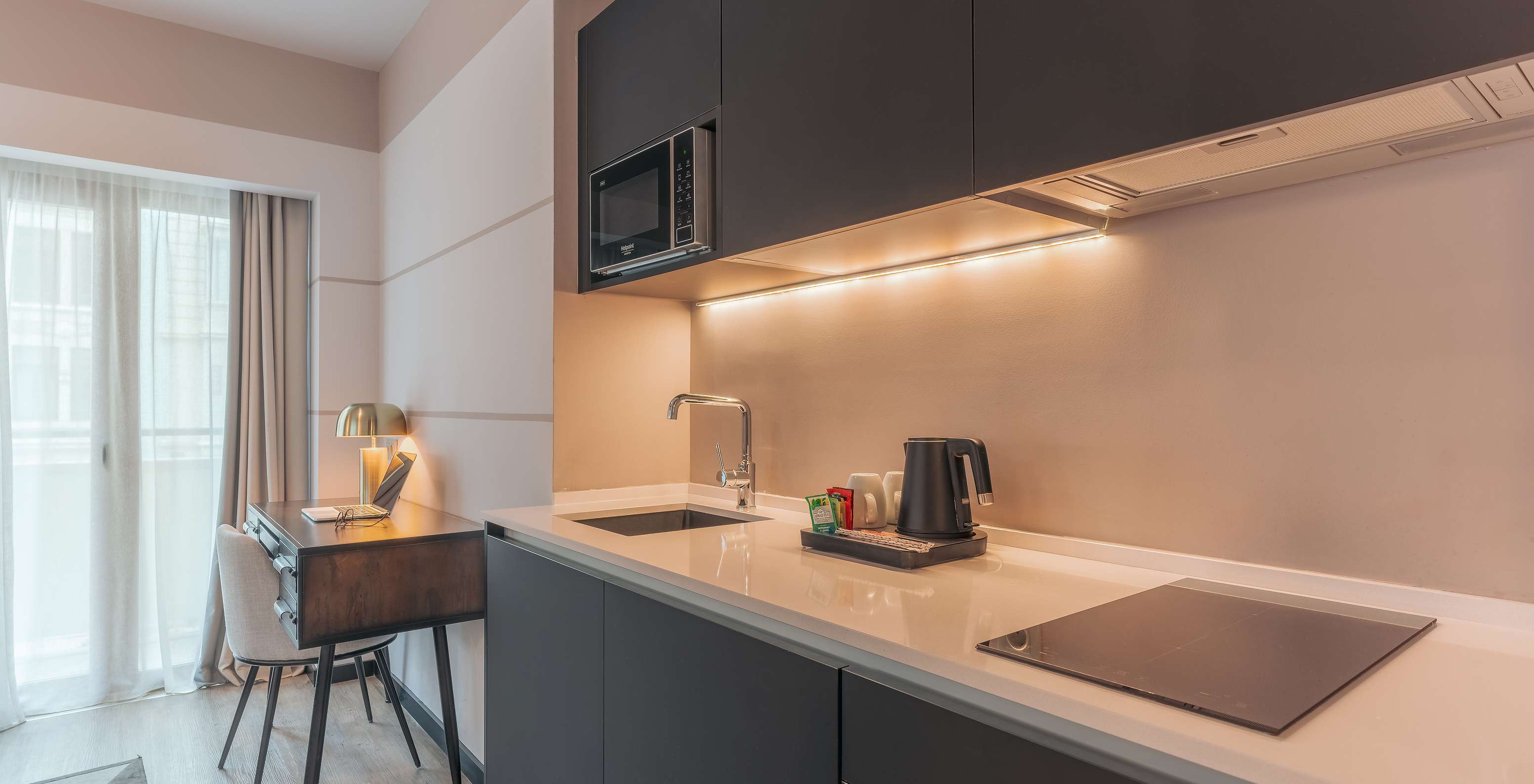 A Junior Suite do Pestana Lisboa Vintage tem um móvel de cozinha com placa de fogão, micro-ondas e uma secretária com cadeira