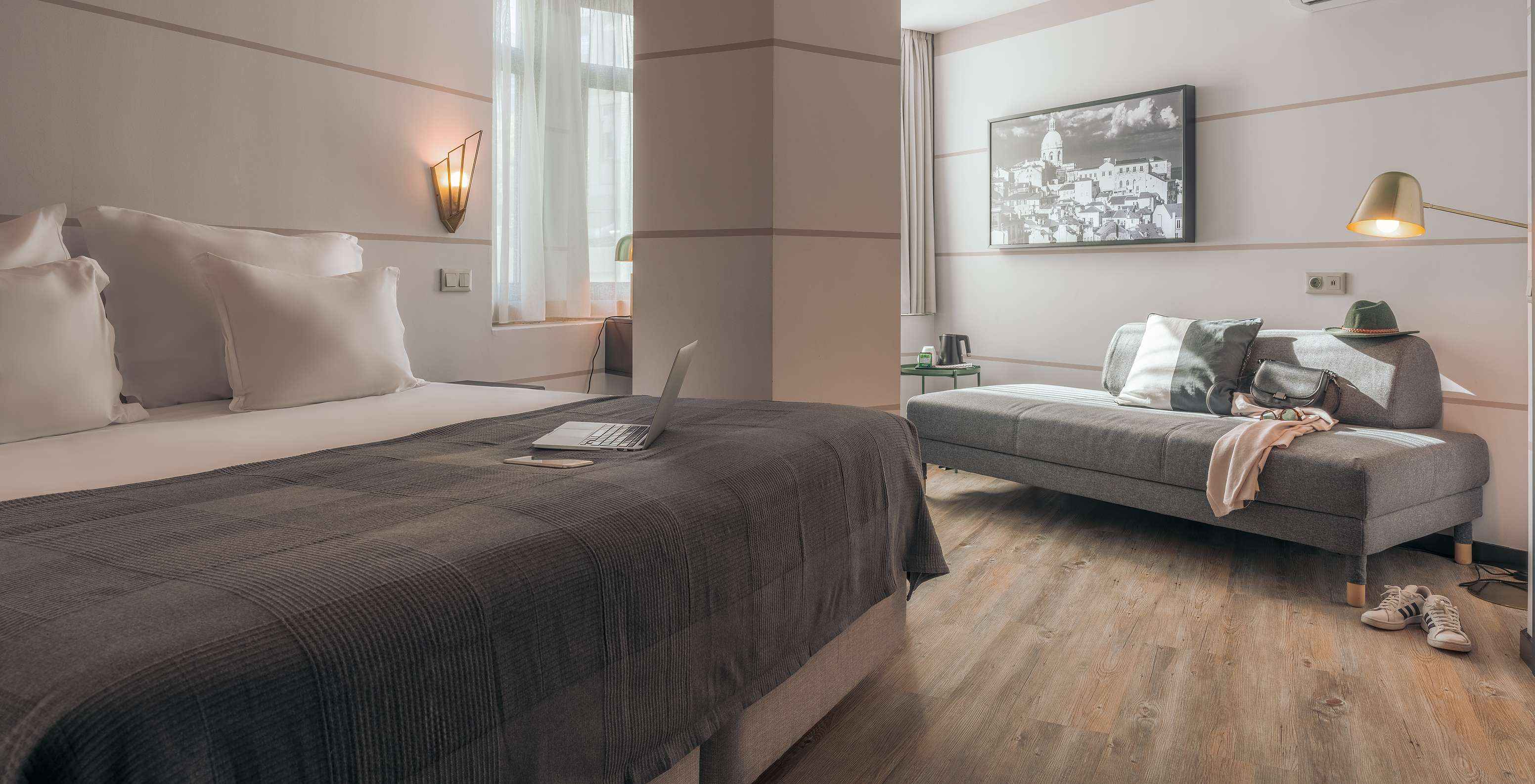 O Double Superior do Pestana Lisboa Vintage tem uma cama de casal com manta cinzenta, um sofá cinzento e uns ténis brancos